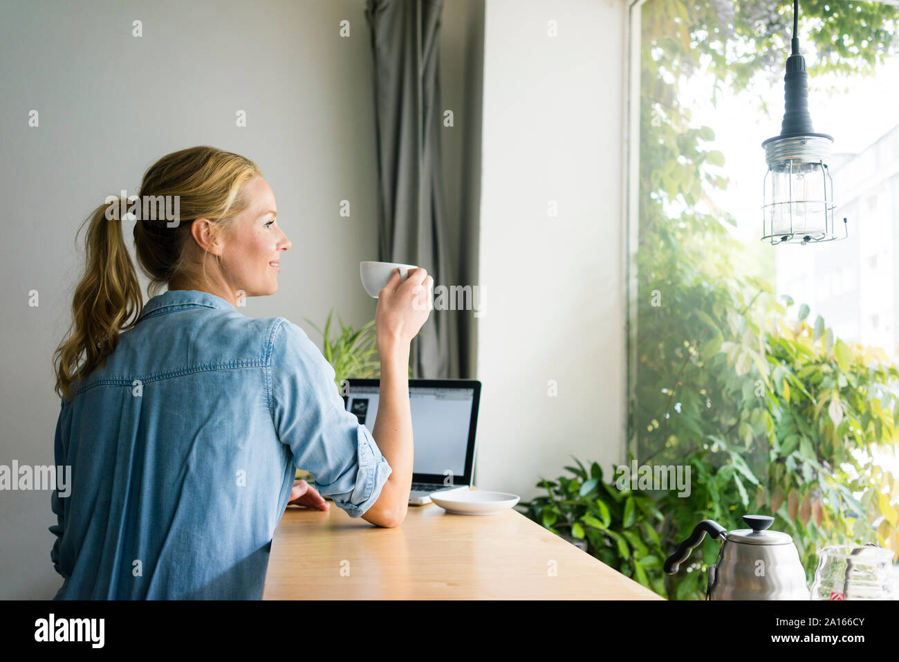 Femme blonde assise dans un café, à l'aide d'un ordinateur portable, de boire du café Banque D'Images