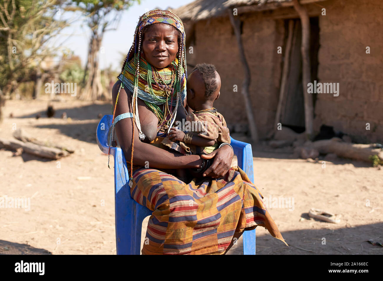 Muhila femme traditionnel assis sur une chaise bleue, avec le bébé sur ses genoux, Congolo, en Angola. Banque D'Images