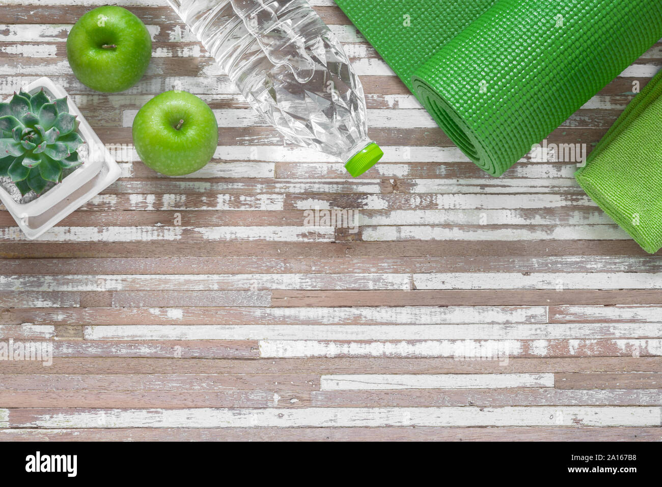 Pour définir la pratique du yoga avec tapis vert, vert, une serviette, une bouteille d'eau et la pomme verte, l'équipement d'exercice sur le bois blanc grunge. Régime alimentaire sain et de concept. Banque D'Images