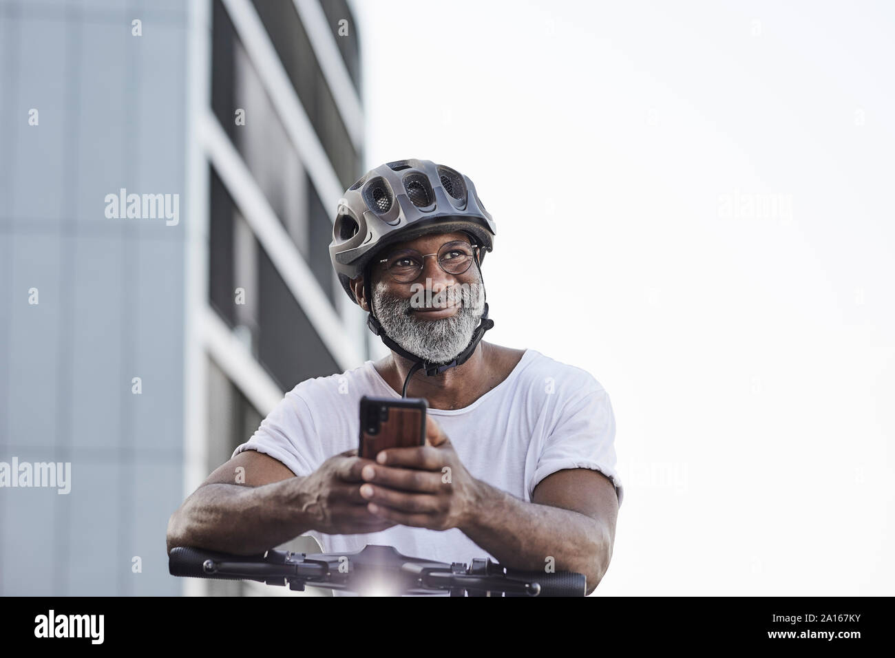 Portrait of happy young man wearing cycling helmet appuyée sur guidon de Scooter électrique Banque D'Images