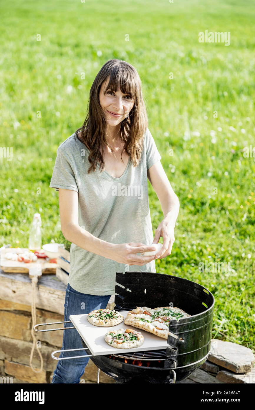 Portrait of smiling woman preparing food sur la grille du barbecue Banque D'Images