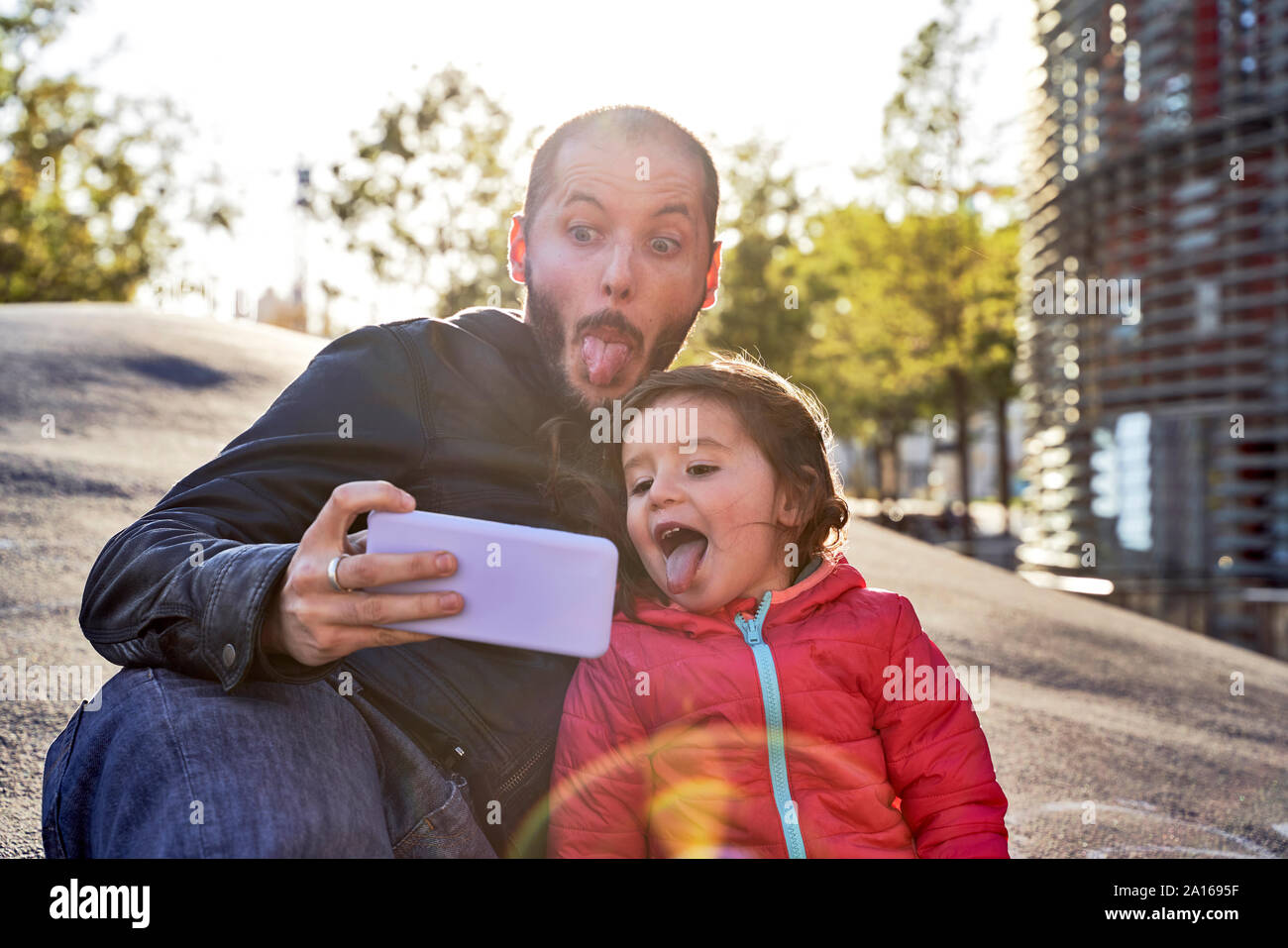 Fillette de deux ans et père de prendre vos autoportraits et pulling faces sur une journée d'hiver au coucher du soleil, Barcelone, Espagne Banque D'Images