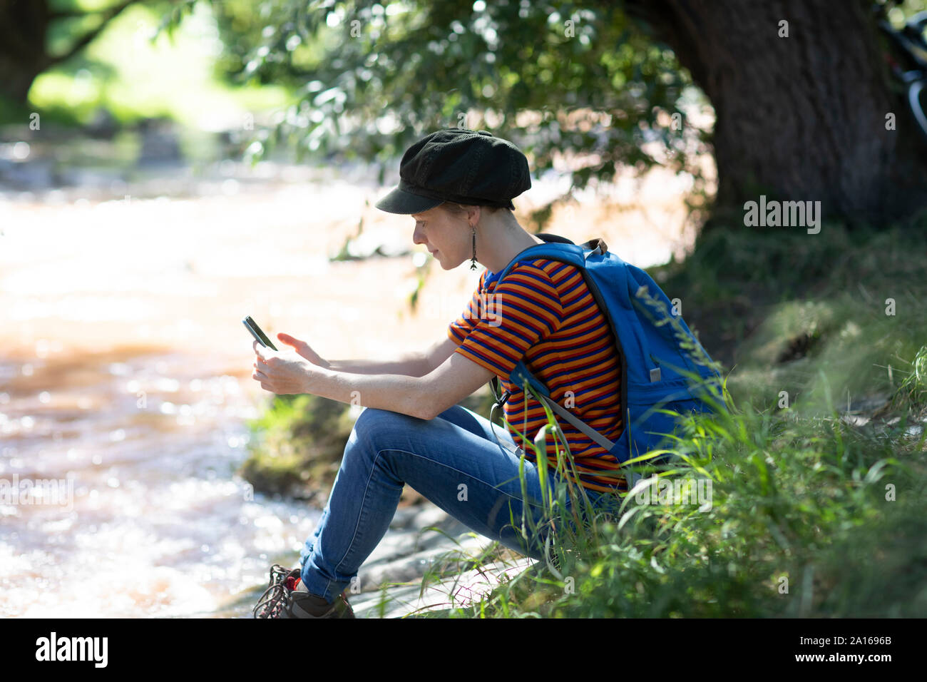 Femme avec sac à dos, assis sur une berge à à son smartphone Banque D'Images