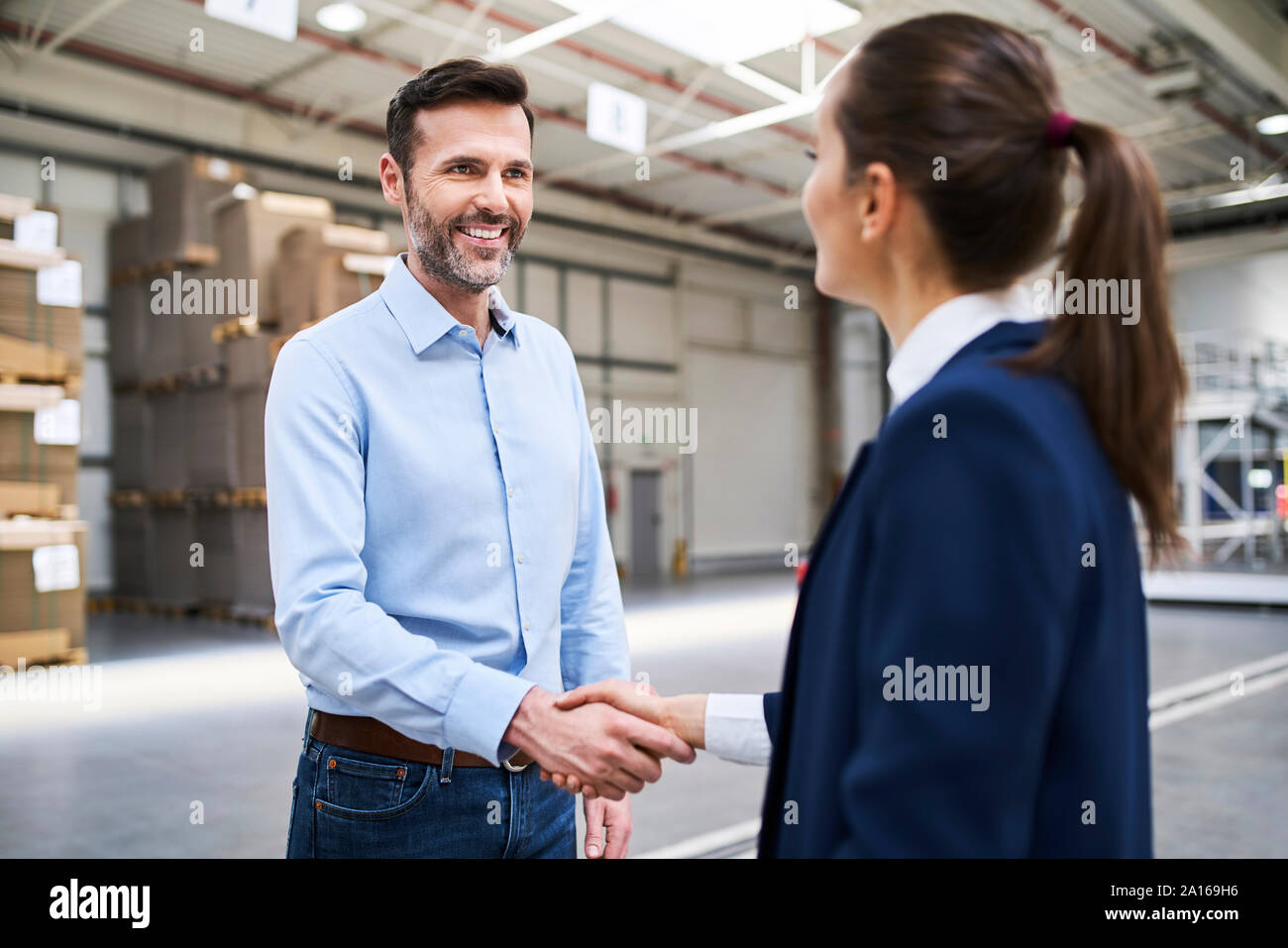 Businessman and businesswoman shaking hands in a factory Banque D'Images