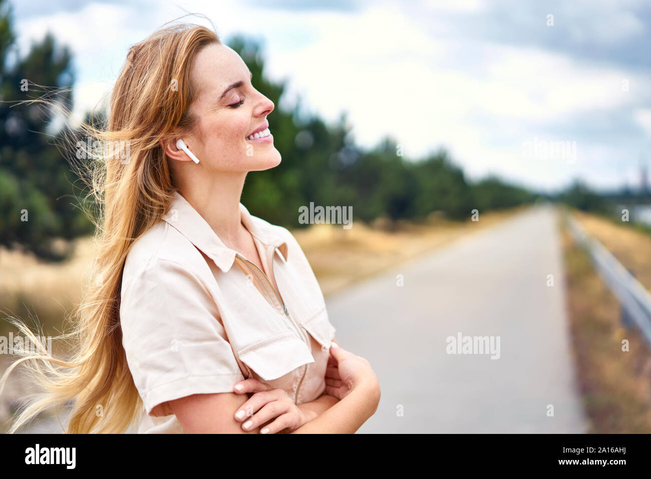 Femme souriante avec des écouteurs sans fil et fermé les yeux dans la nature Banque D'Images Femme souriante avec des écouteurs sans fil et fermé les yeux dans la nature Banque D'Images