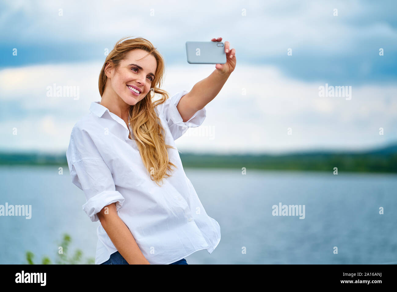 Happy woman with smartphone selfies au bord de lac Banque D'Images Happy woman with smartphone selfies au bord de lac Banque D'Images