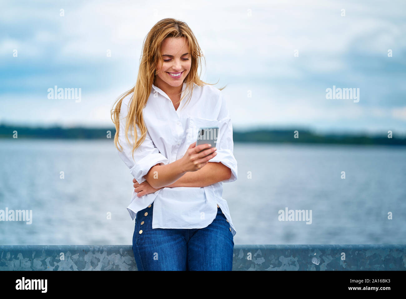 Happy woman checking cell phone au bord de lac Banque D'Images Happy woman checking cell phone au bord de lac Banque D'Images