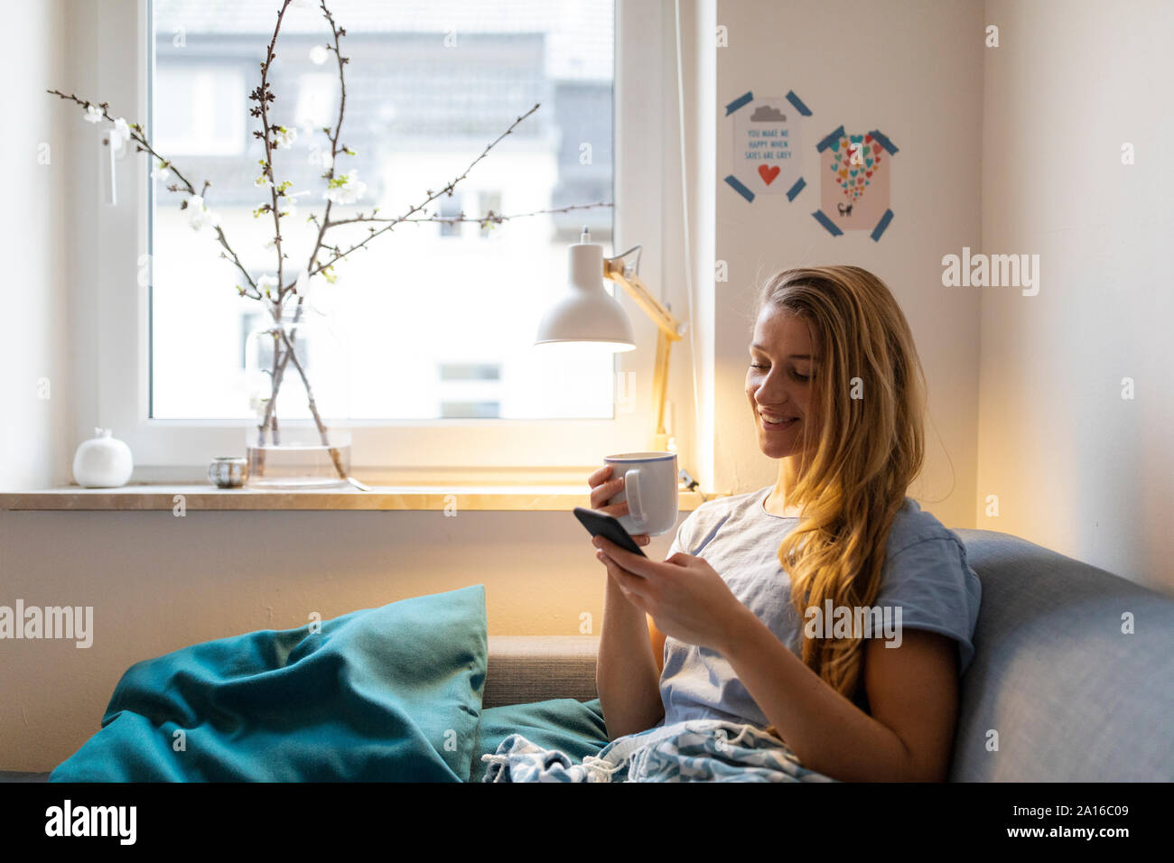 Young woman using cell phone on sofa at home Banque D'Images