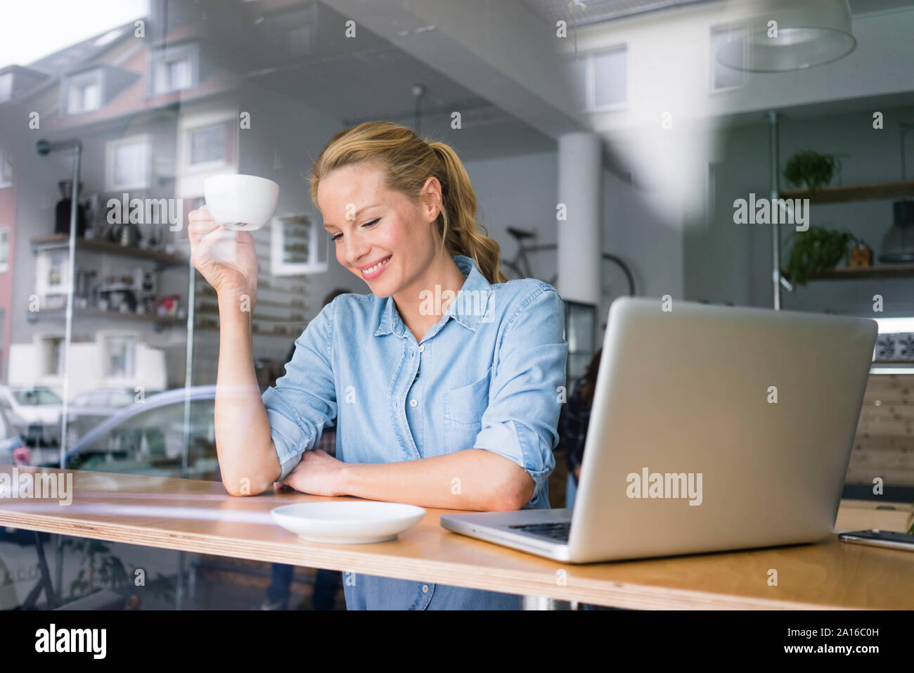 Femme blonde assise dans un café, à l'aide d'un ordinateur portable, de boire du café Banque D'Images