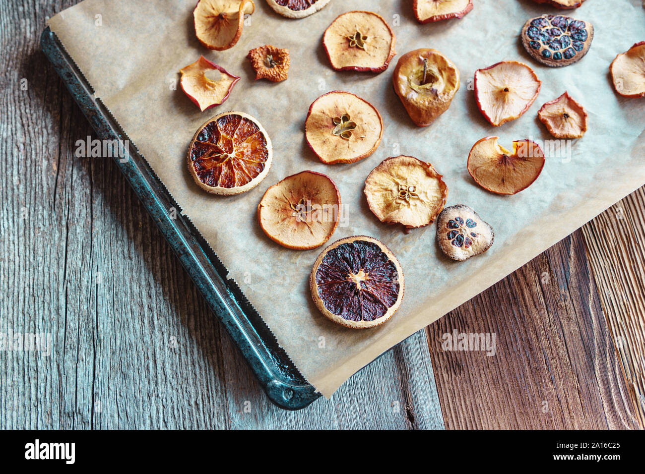 Des tranches de pommes et oranges séchées sur du papier sulfurisé et la plaque de cuisson, arrangement diagonal, fond de bois - vue oblique, format horizontal Banque D'Images