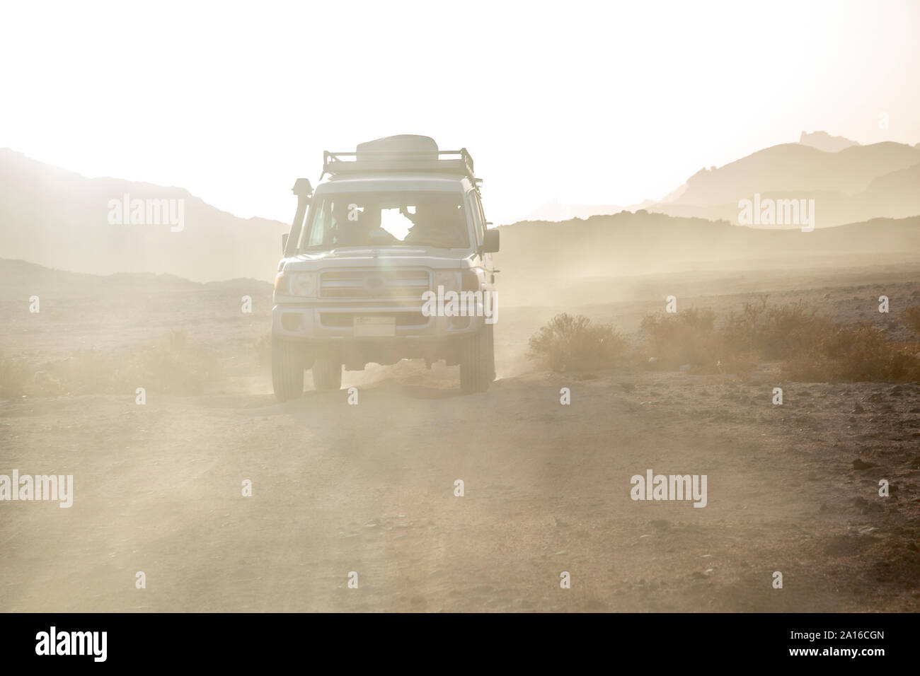 Véhicule hors route sur chemin de terre au milieu de la poussière dans le ciel du désert contre pendant le coucher du soleil Banque D'Images