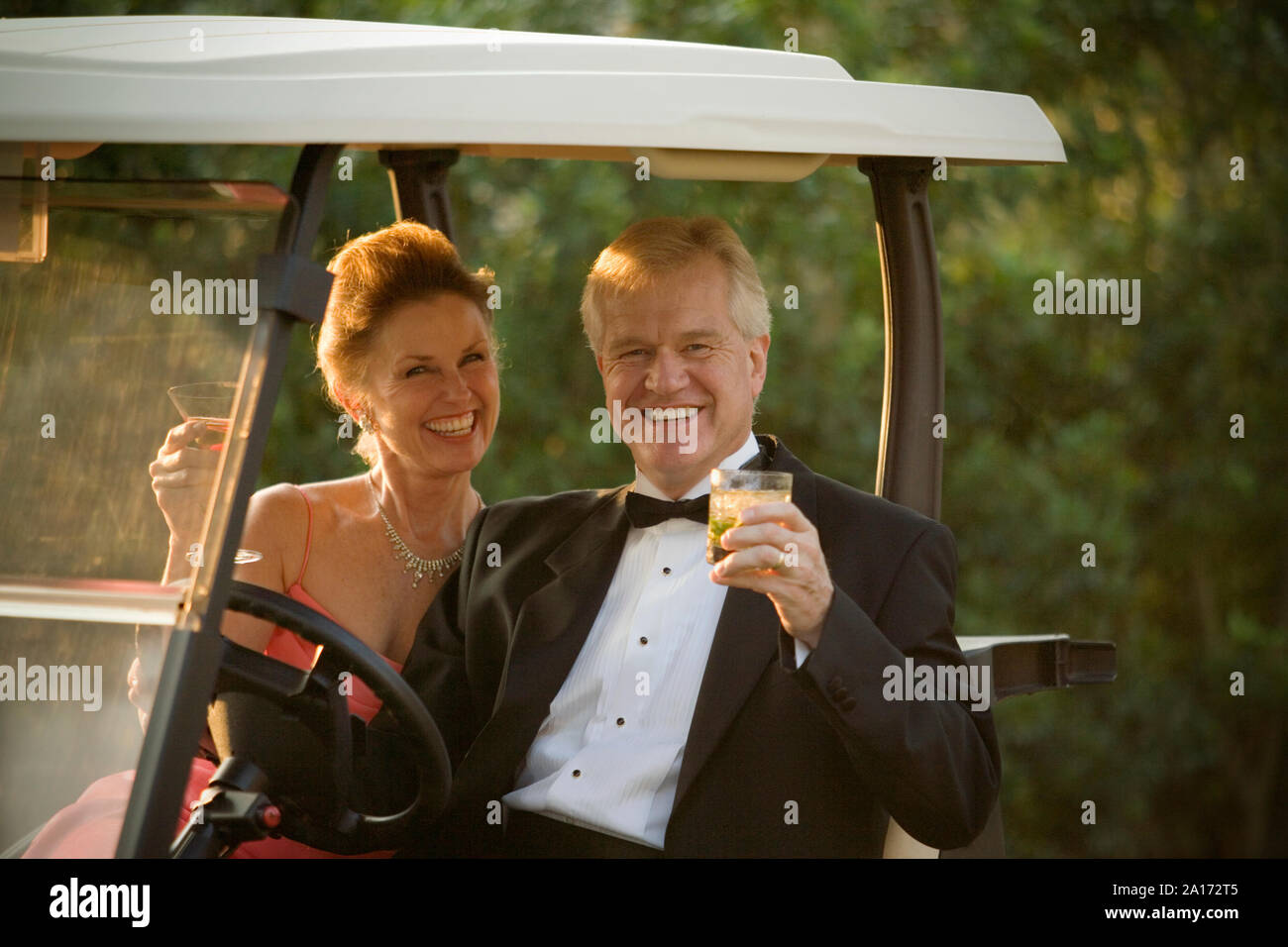 Portrait of a young couple officiellement habillé assis sur un chariot de golf avec des cocktails. Banque D'Images