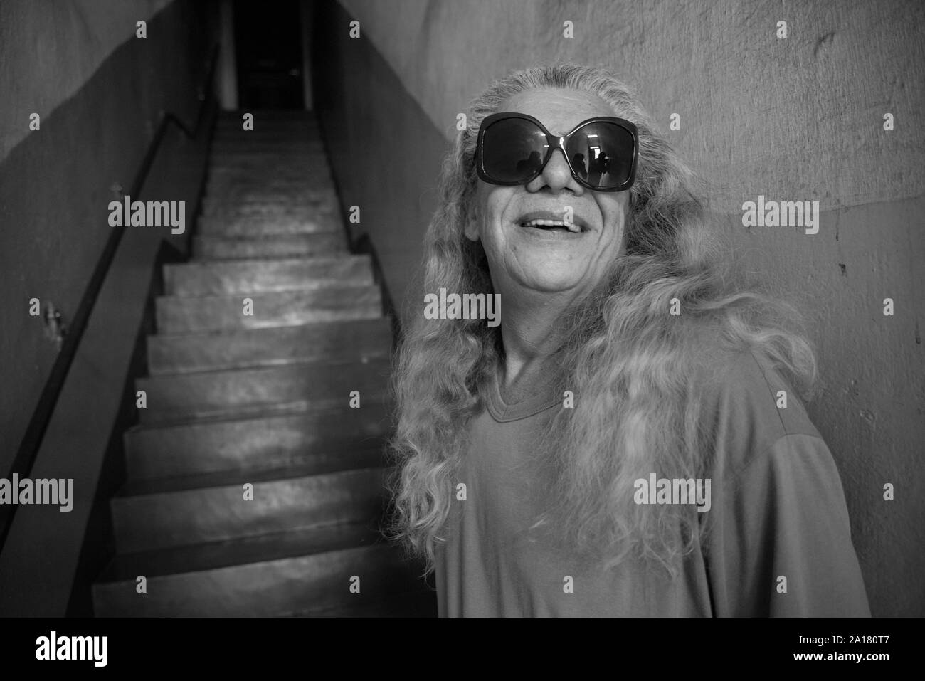 Transgenre avec de grandes lunettes de soleil souriant sur un escalier Banque D'Images
