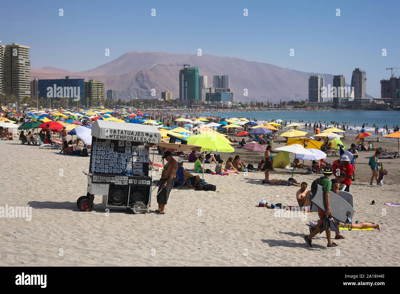 IQUIQUE, CHILI - 23 janvier 2015 : un homme tirant une charrette à travers le sable offrant des tatouages temporelles sur la plage Cavancha bondé à Iquique Banque D'Images