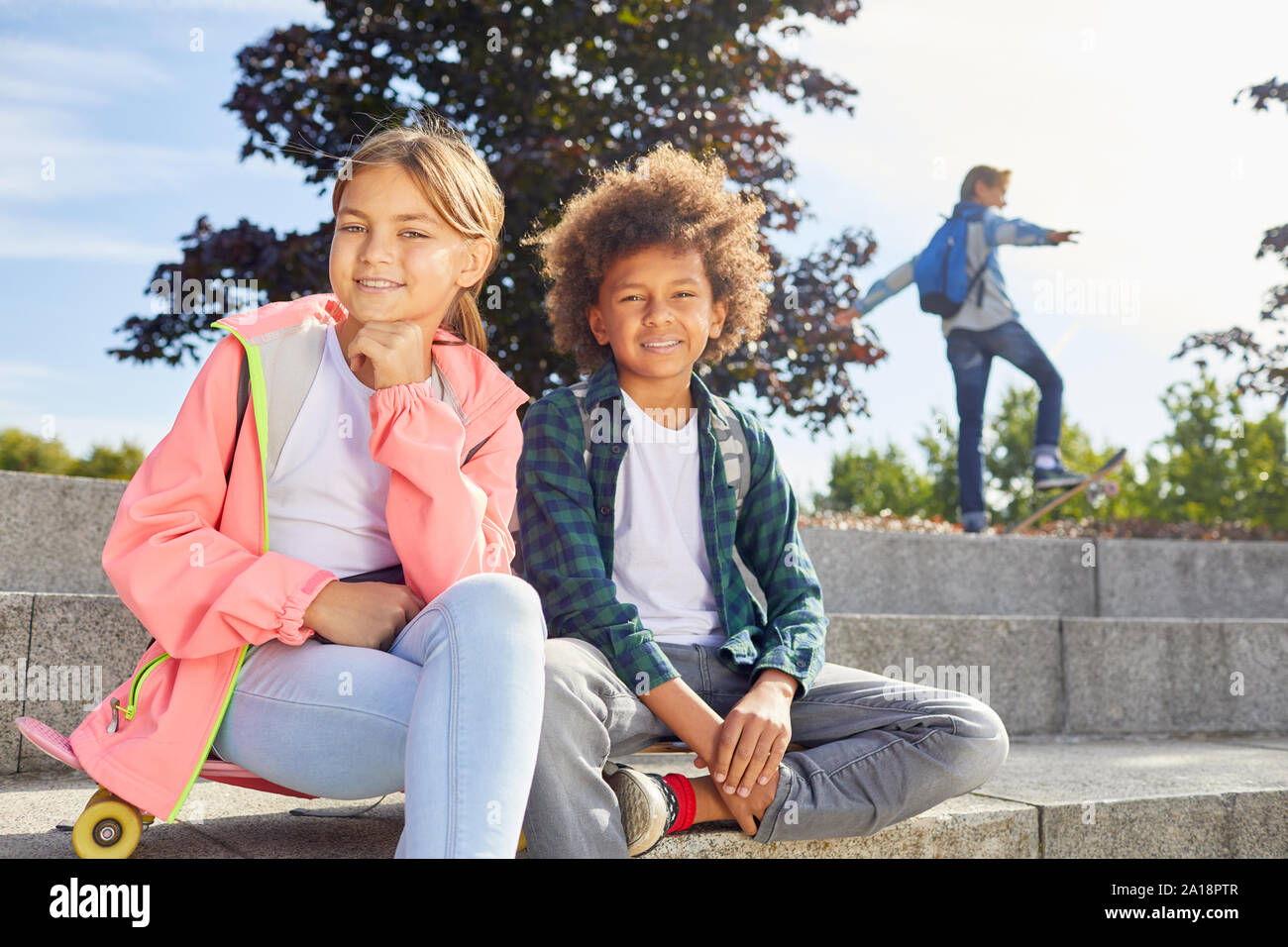 Portrait of cute girl sitting avec African boy et ils smiling at camera tout en vous reposant sur l'escalier extérieur Banque D'Images