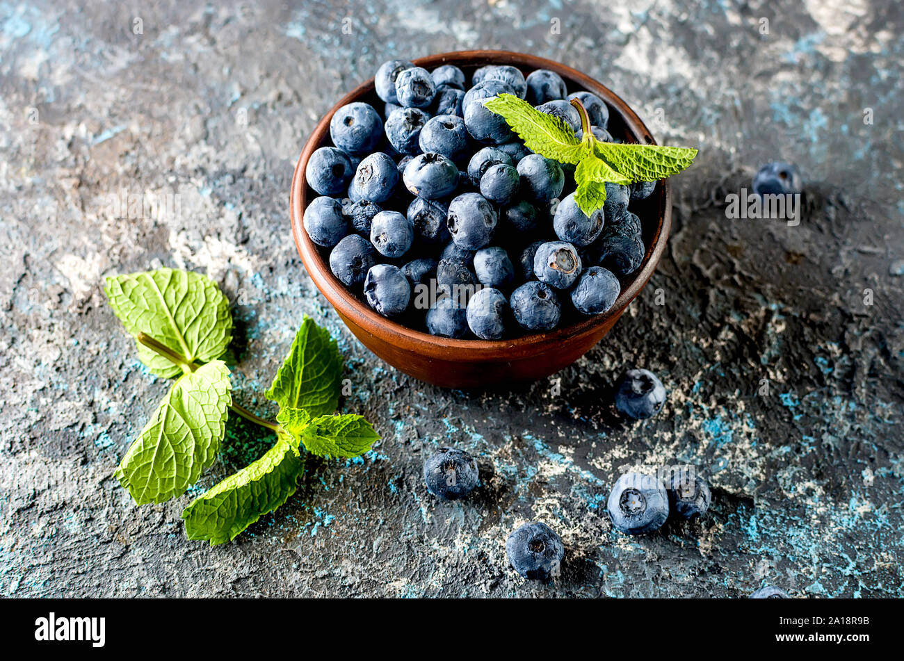 Les bleuets mûrs en ceramik bol avec menthe feuilles sur un fond de béton foncé Banque D'Images