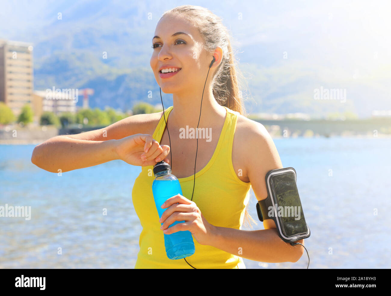 Athlète féminine joyeux heureux avec brassard pour téléphone intelligent ouvrir bouteille de boisson d'après l'entraînement quotidien et à la route à l'extérieur. Banque D'Images