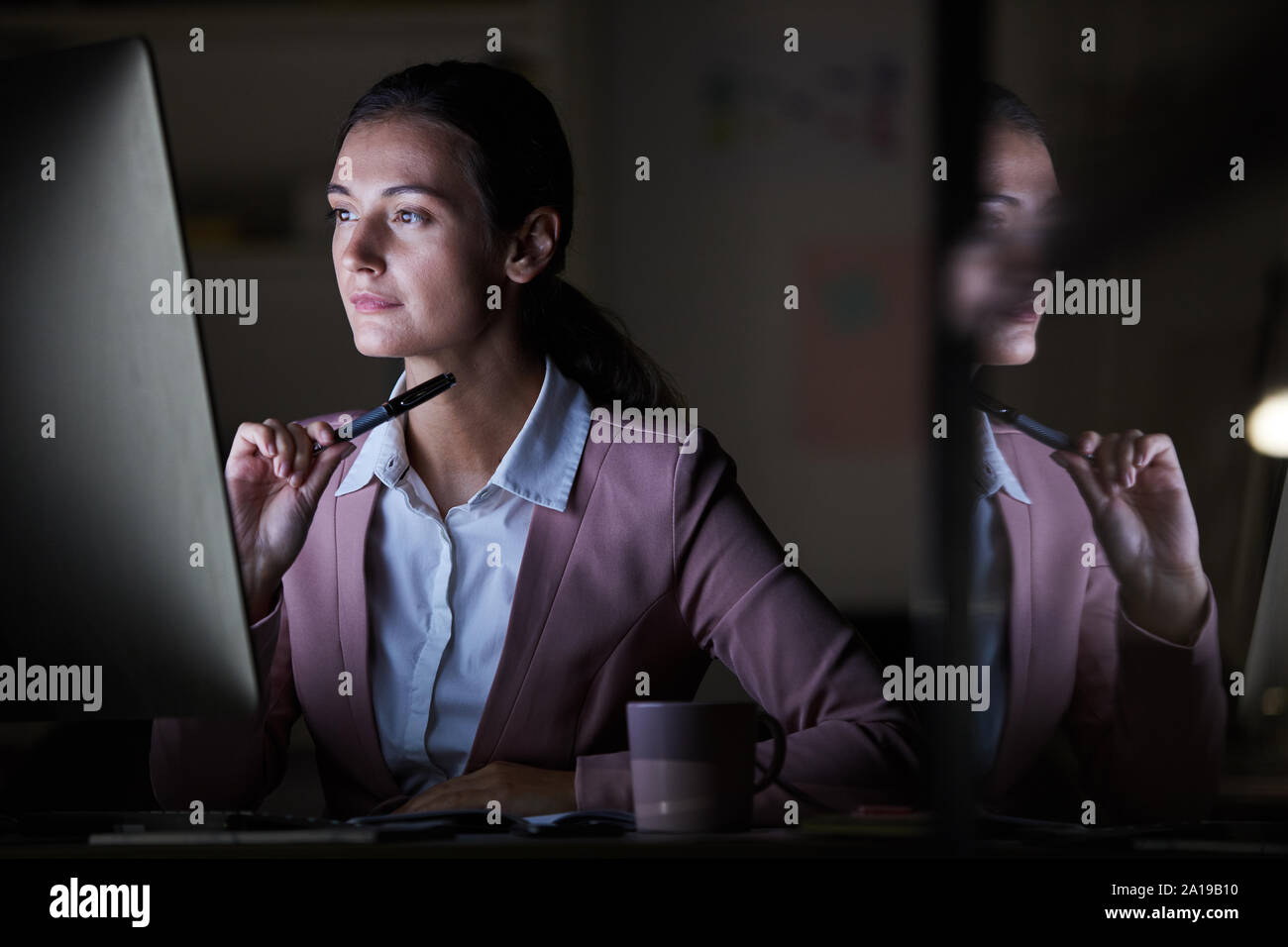 Les jeunes concentrés à manager au moniteur de l'ordinateur tout en travaillant à son travail jusqu'au soir à l'office de tourisme Banque D'Images
