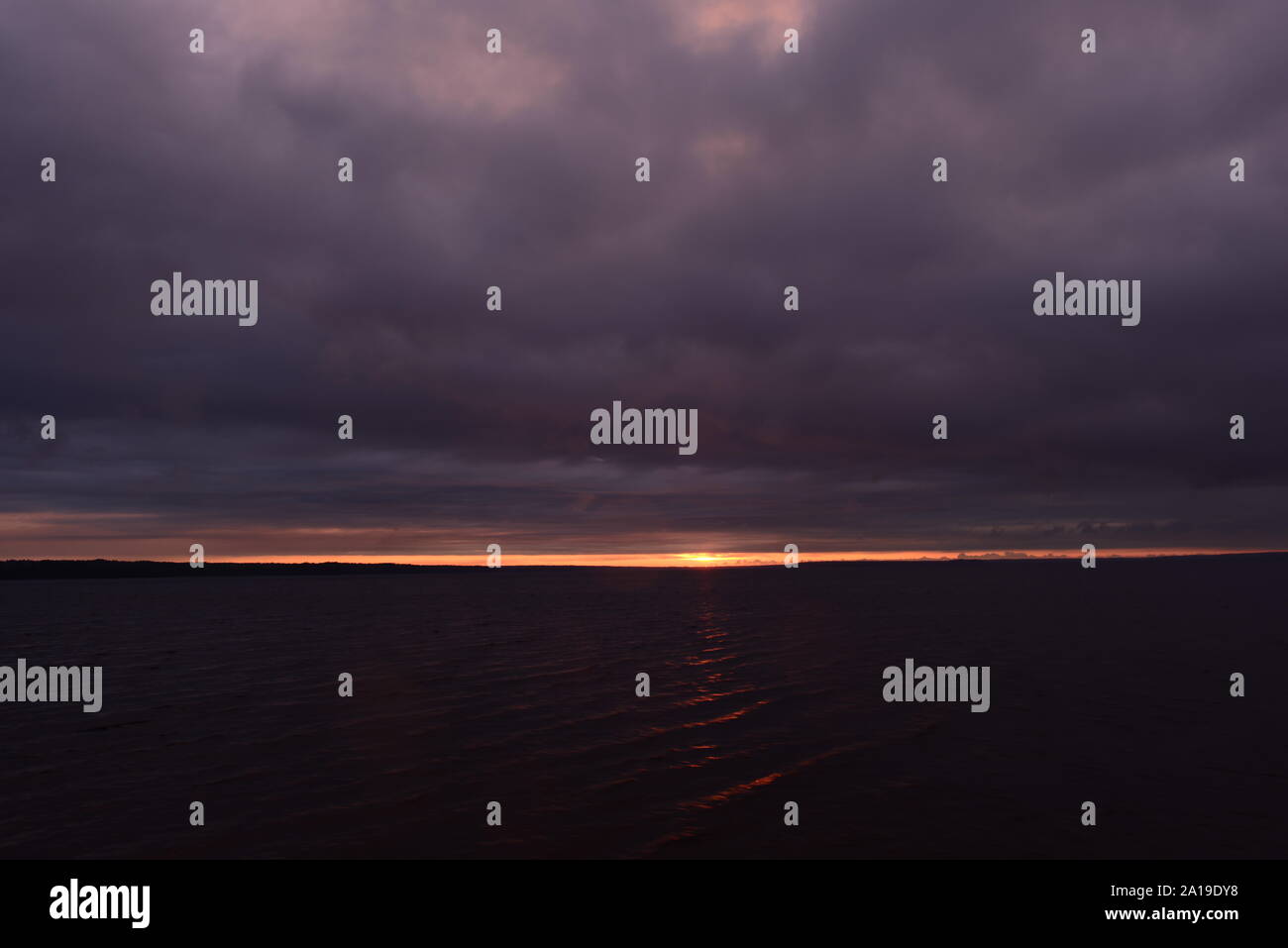 Sunbeam de nuages orageux au coucher du soleil sur une surface sombre de l'eau Banque D'Images