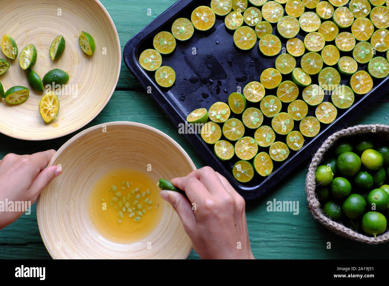 Vue supérieure de la part des gens de squeeze fruits kumquat dans bol en bois qui réduit de moitié sur peel vert et jaune de la chair, cette riche de fruits aigres vitami Banque D'Images