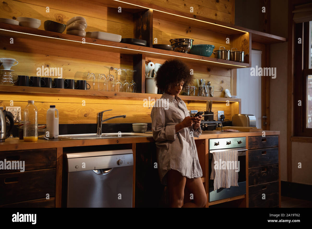 Young woman using smartphone in kitchen Banque D'Images