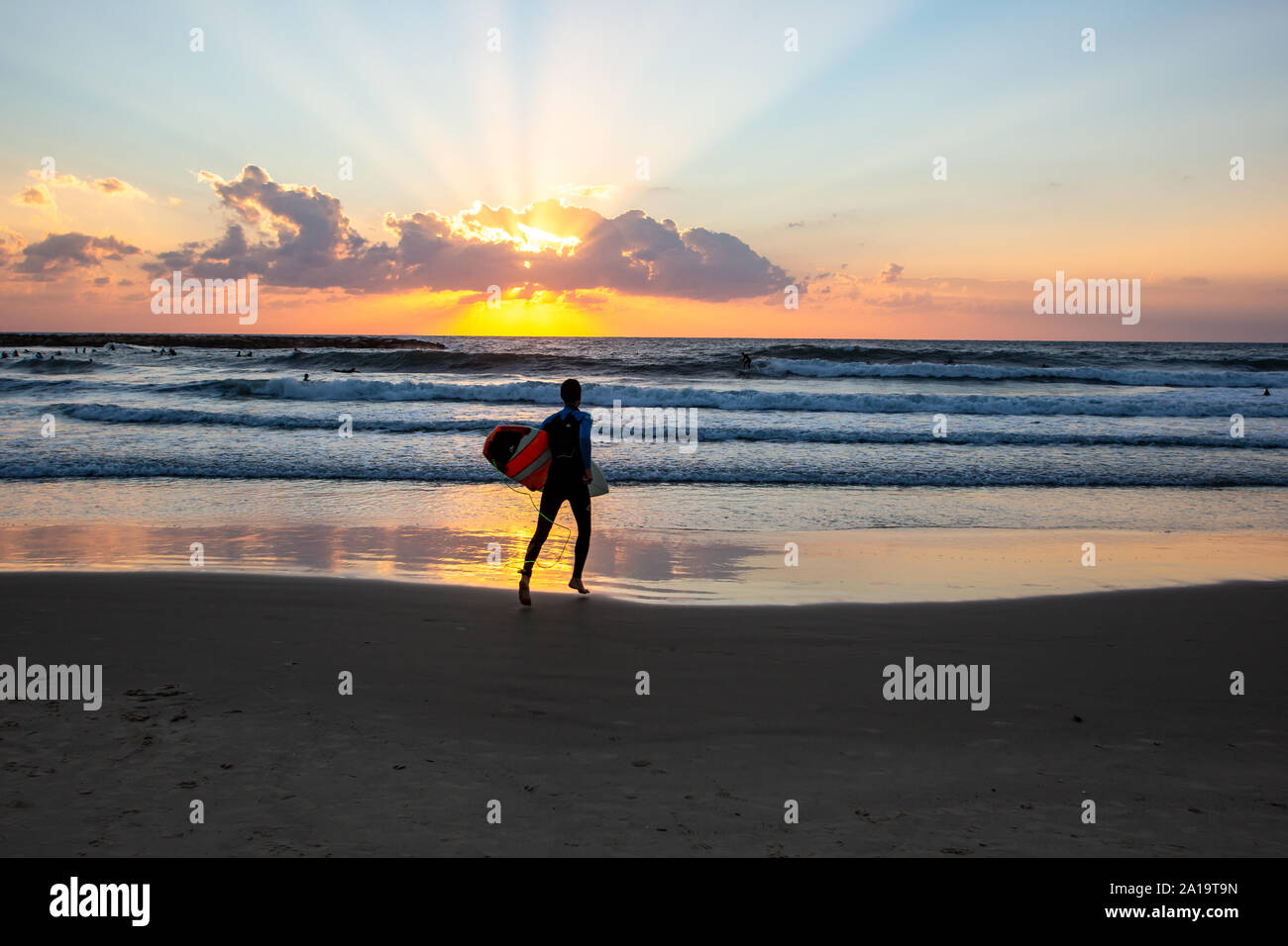Un type avec un surf sur la plage au coucher du soleil de Tel Aviv Banque D'Images