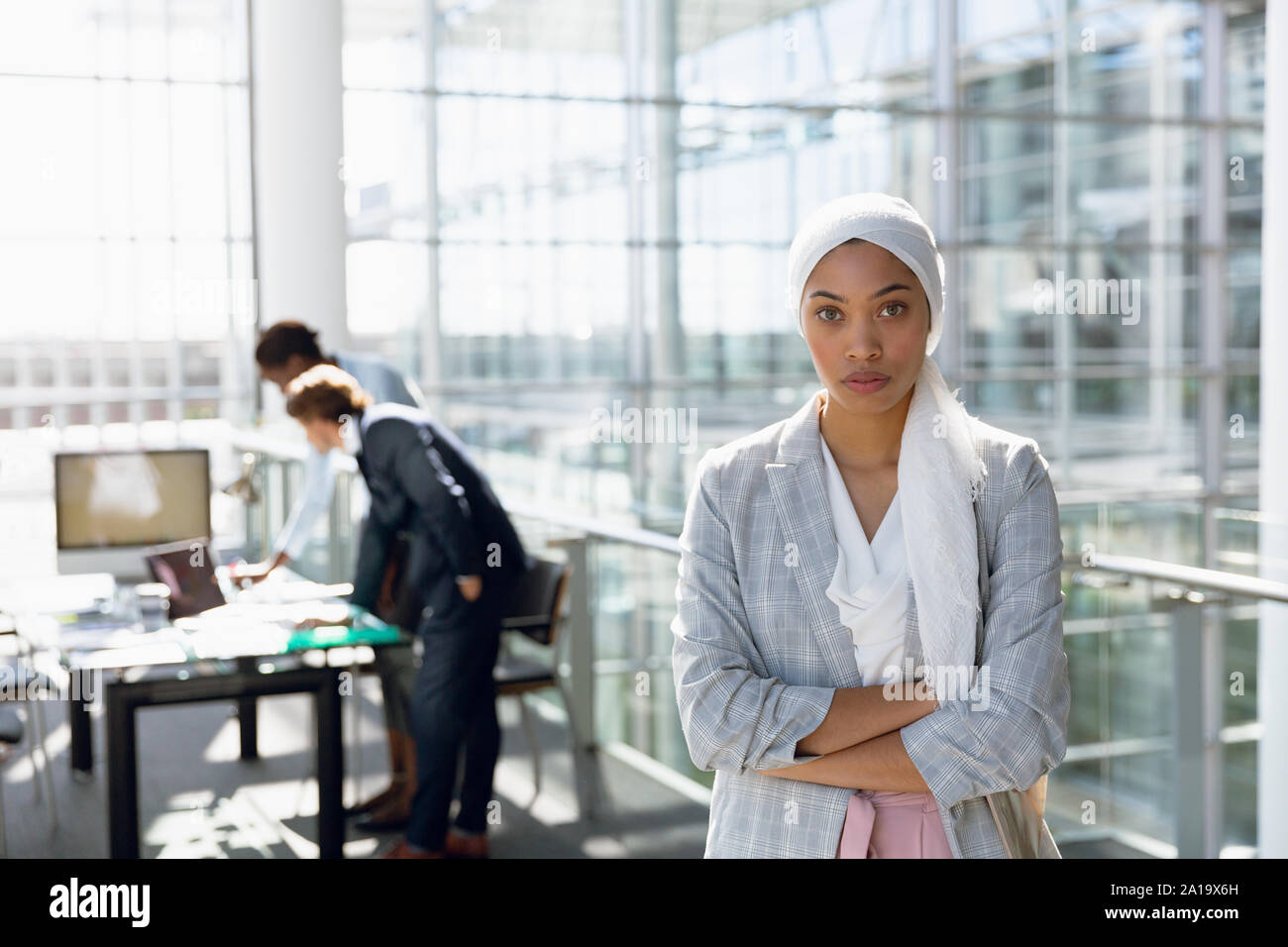 Businesswoman in hijab debout avec les bras croisés pendant que ses collègues qui travaillent en arrière-plan Banque D'Images