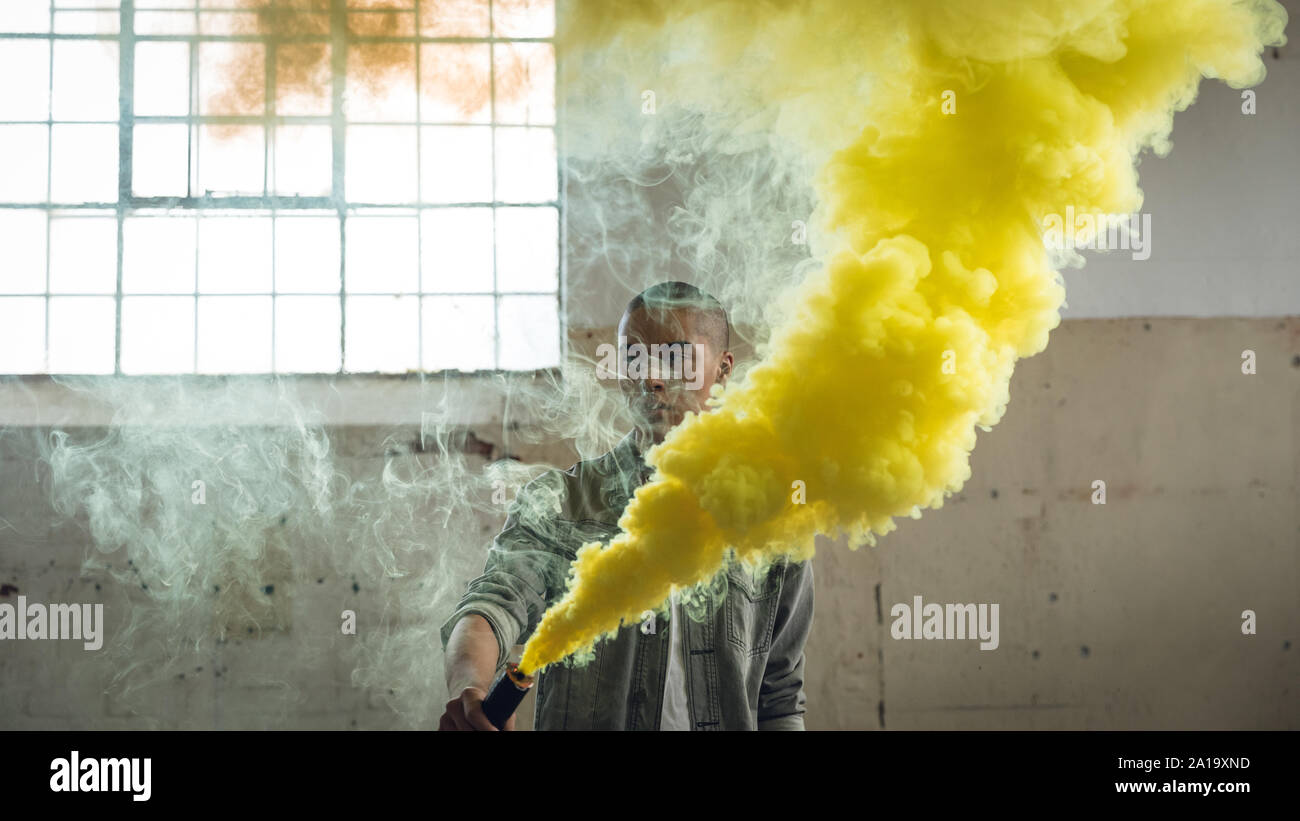 Jeune homme tenant une bouilloire de fumée fumée jaune produisant Banque D'Images