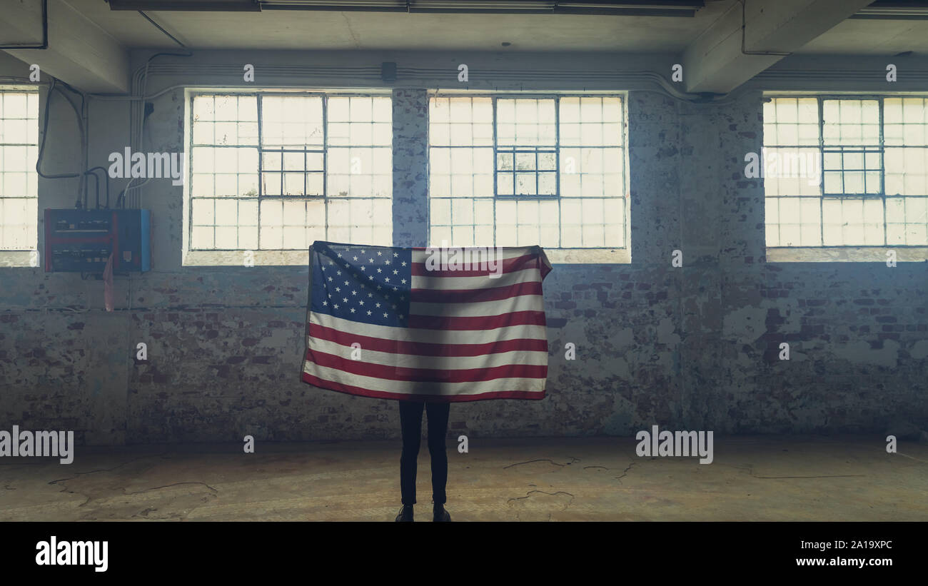Jeune homme tenant un drapeau américain à l'intérieur d'un entrepôt vide Banque D'Images