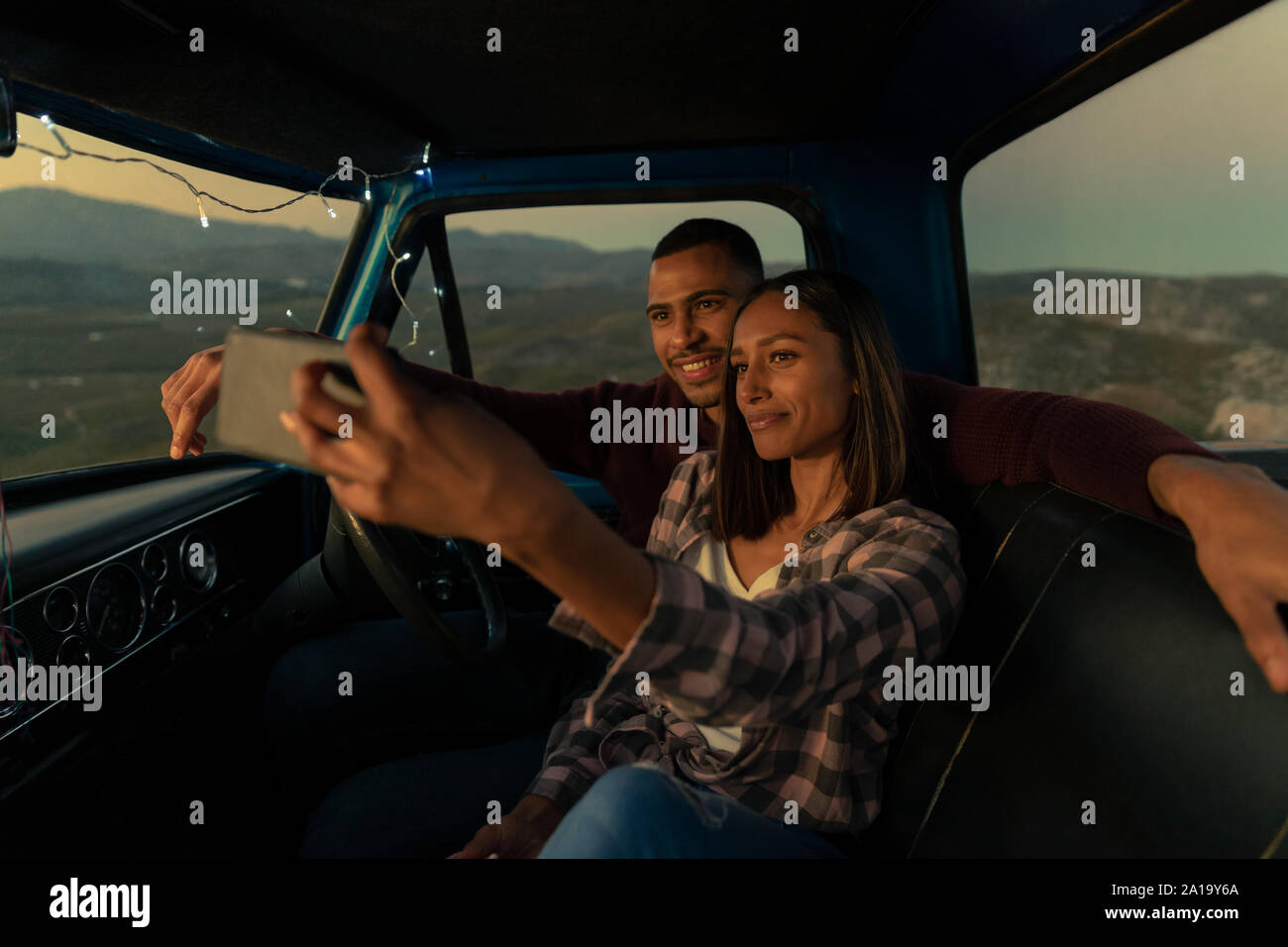 Jeune couple sur un voyage par la route en prenant un dans leur voiture selfies at Dusk Banque D'Images