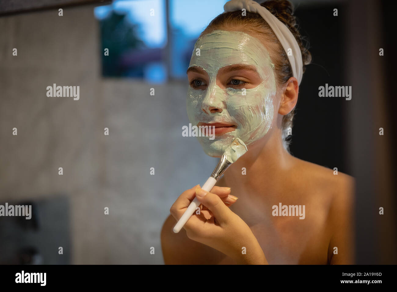 Jeune femme l'application d'un masque de visage dans une salle de bains moderne Banque D'Images
