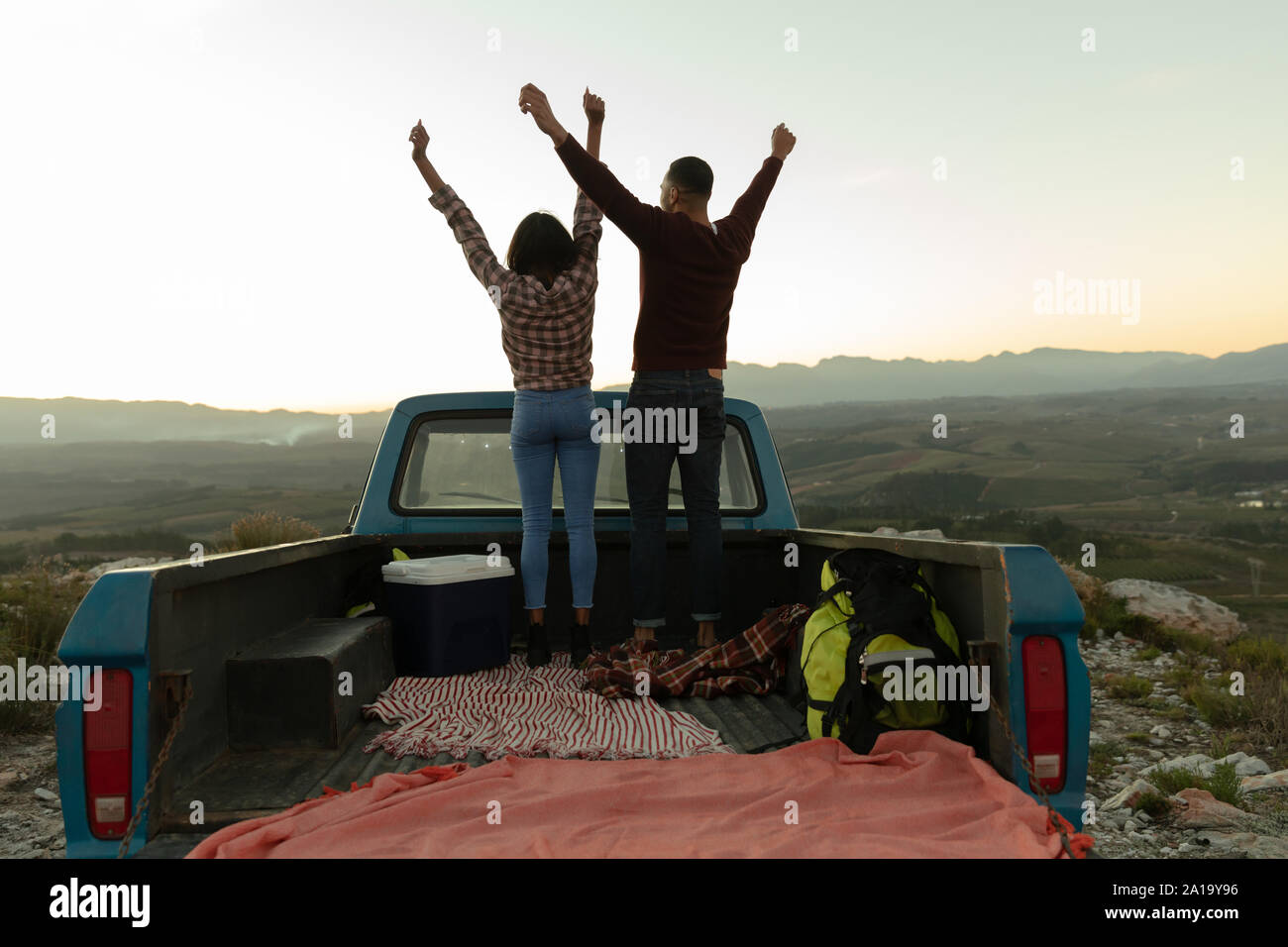 Jeune couple sur un voyage sur la route debout sur leur camion au coucher du soleil Banque D'Images