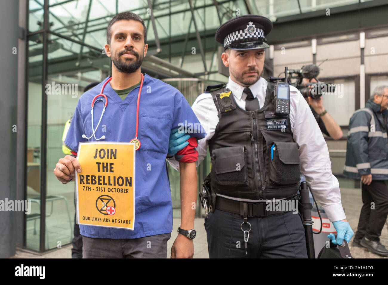 Londres, Royaume-Uni. 25 septembre 2019. Un professionnel de la santé en gommages médicaux et stéthoscope est escorté hors des lieux par un officier de la police métropolitaine lors d'une manifestation climatique extinction Rebellion devant le Department for Business, Energy & Industrial Strategy (BEIS) à Londres. La manifestation met en lumière la crise de santé publique imminente causée par le changement climatique. L’activiste porte une pancarte jaune indiquant « REBELLION 7TH - 21ST OCTOBER NOS VIES SONT EN JEU » avec le logo extinction Rebellion. Les médias et autres observateurs sont présents. Penelope Barritt/Alamy Live News Banque D'Images