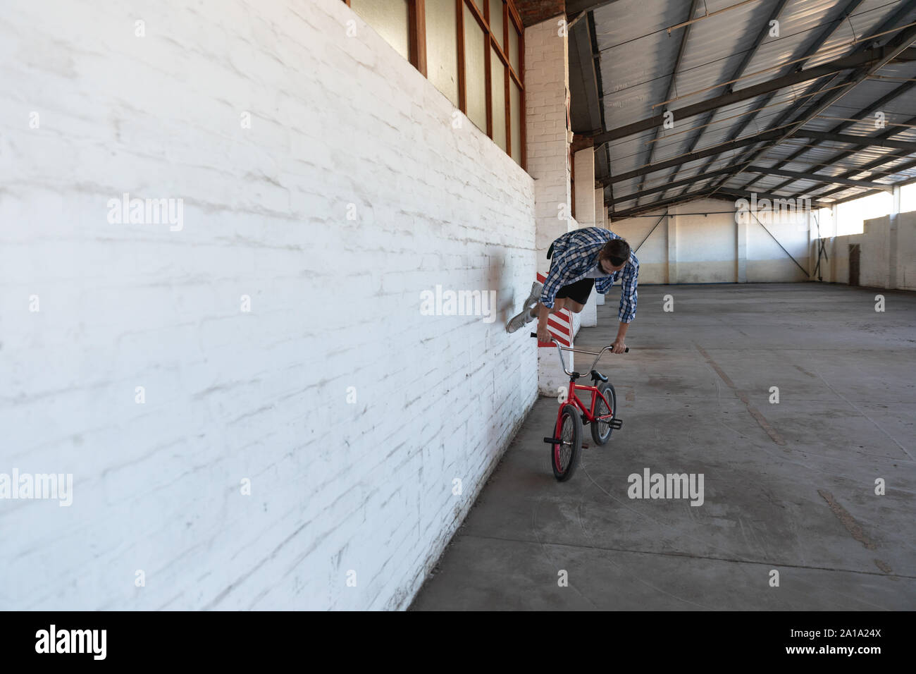 Le BMX rider exécute sur mur dans un entrepôt vide Banque D'Images