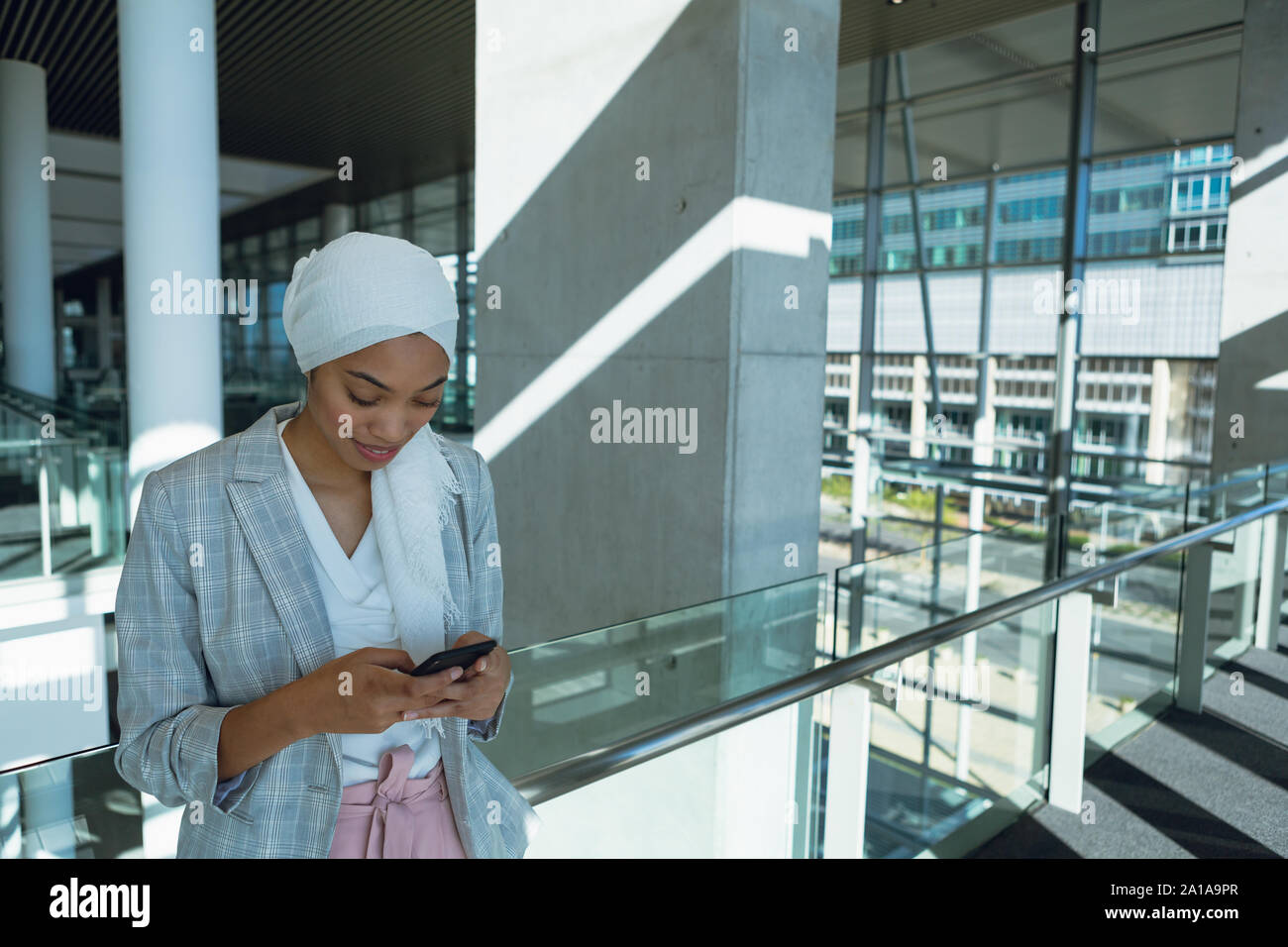 En hijab Businesswoman leaning on railing et à l'aide de téléphone mobile dans le couloir au bureau moderne Banque D'Images
