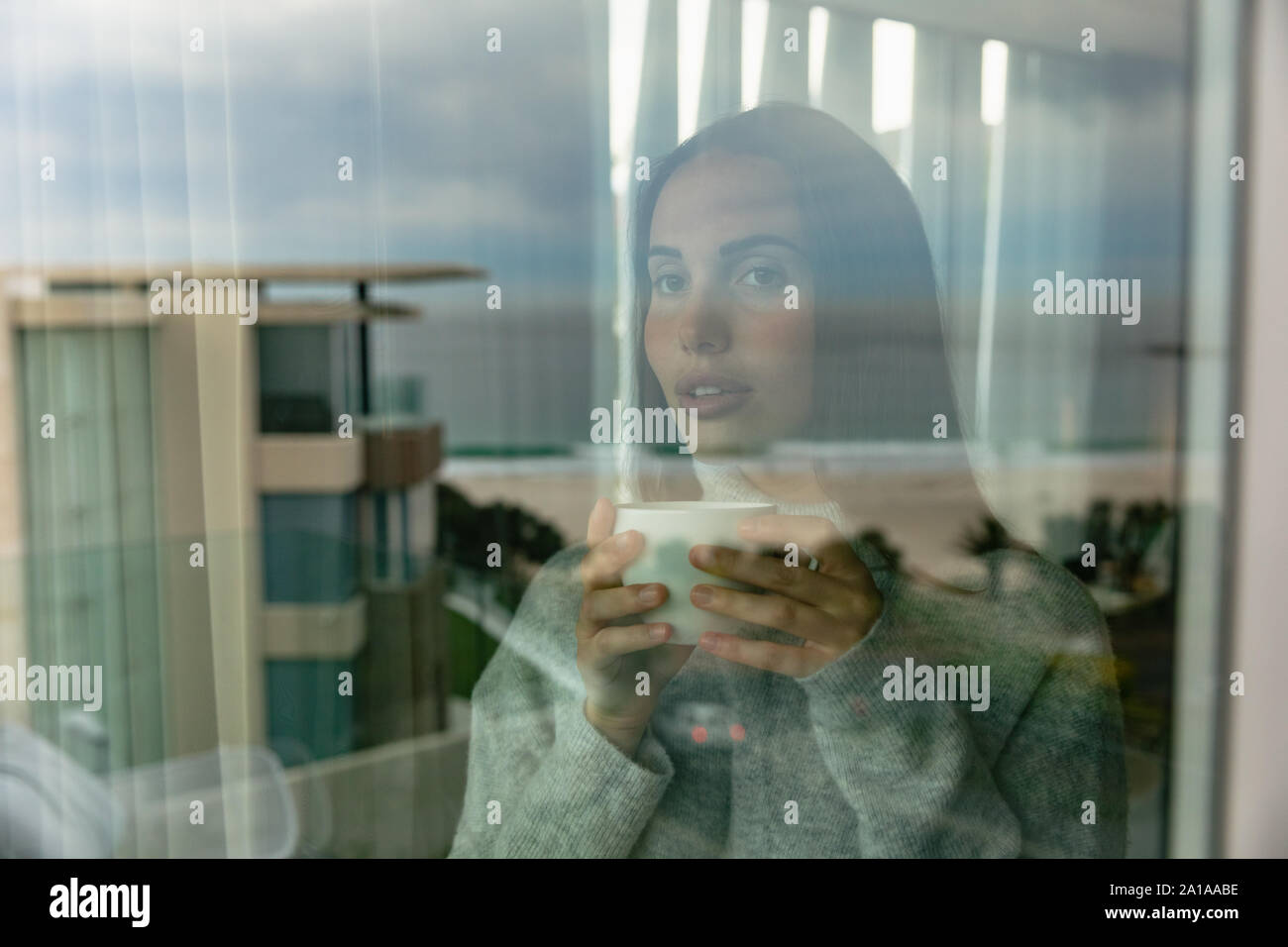 Jeune femme tenant une tasse de café à la fenêtre de Banque D'Images