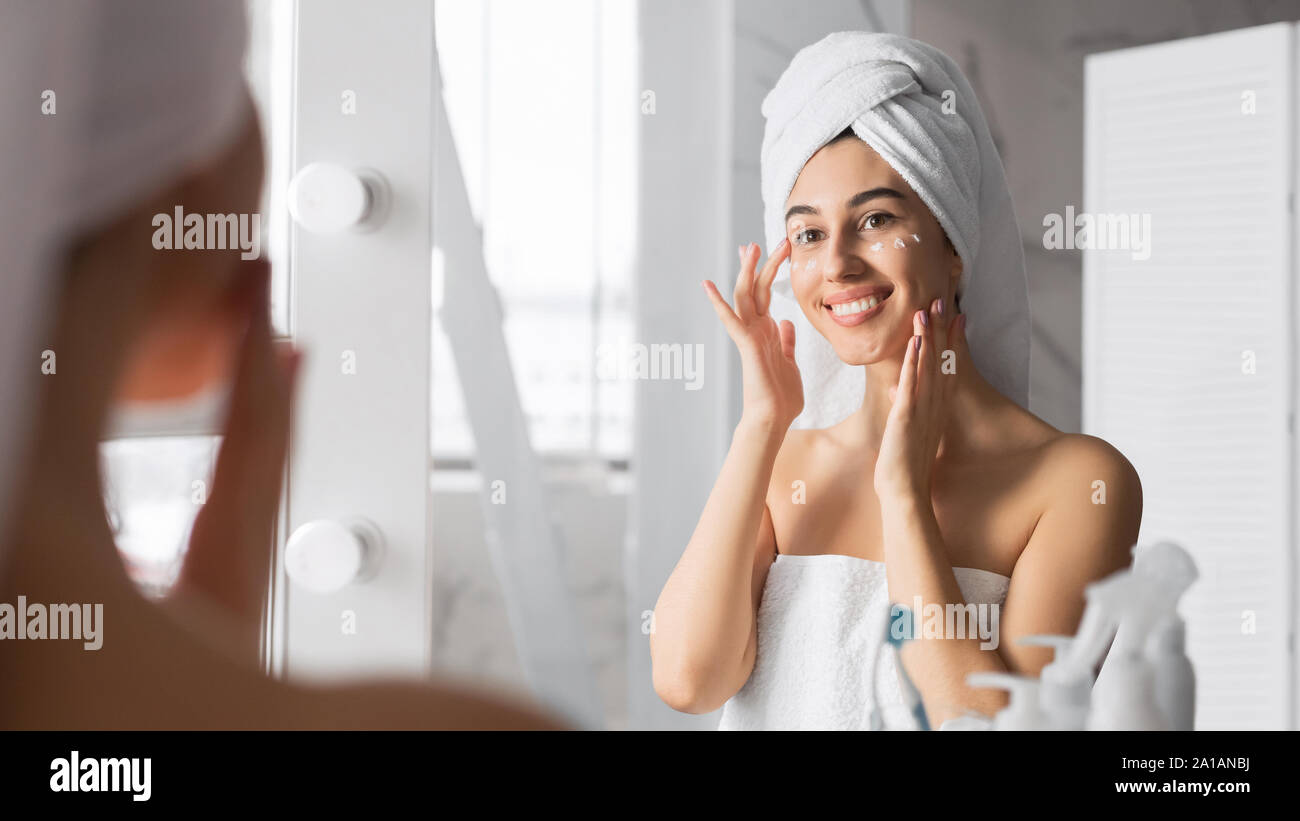 Woman Applying Eye Cream en prenant soin de peau dans la salle de bains Banque D'Images