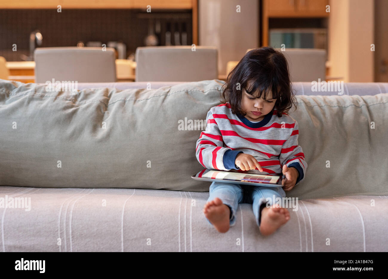 Petite fille assise sur son canapé à l'aide d'une tablette numérique Banque D'Images