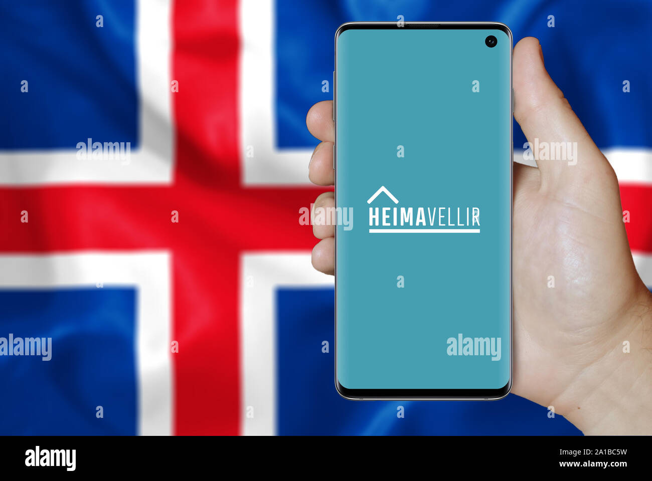 Un homme est titulaire d'un smartphone affichant le logo de société Heimavellir cotée au Nasdaq l'Islande. Drapeau islandais dans l'arrière-plan. Credit : PIXDUCE Banque D'Images