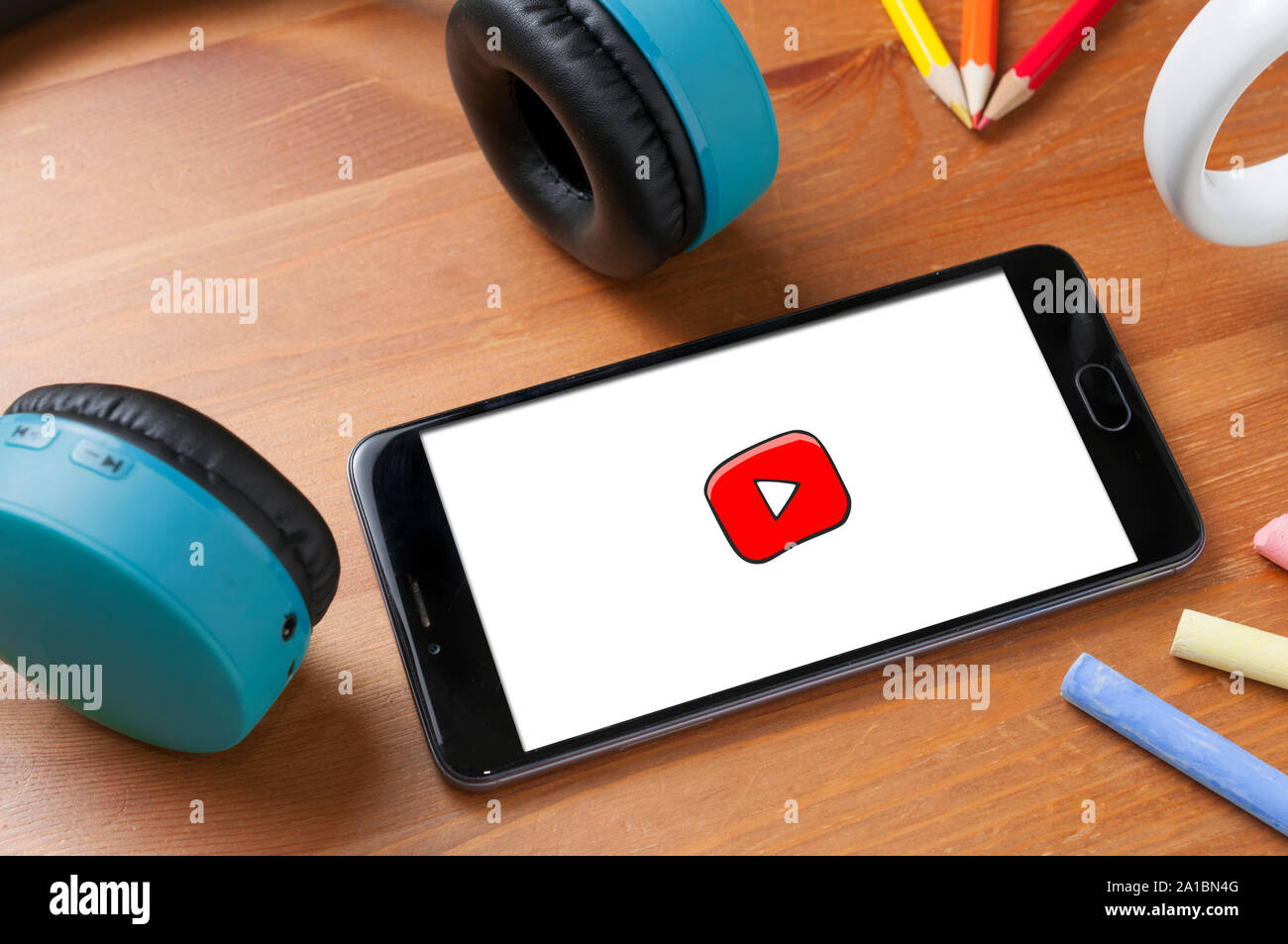 Carrara, Italie - 25 septembre 2019 : Smartphone avec Youtube Kids logo sur table en bois à côté d'une paire d'écouteurs sans fil, des crayons et des cha Banque D'Images