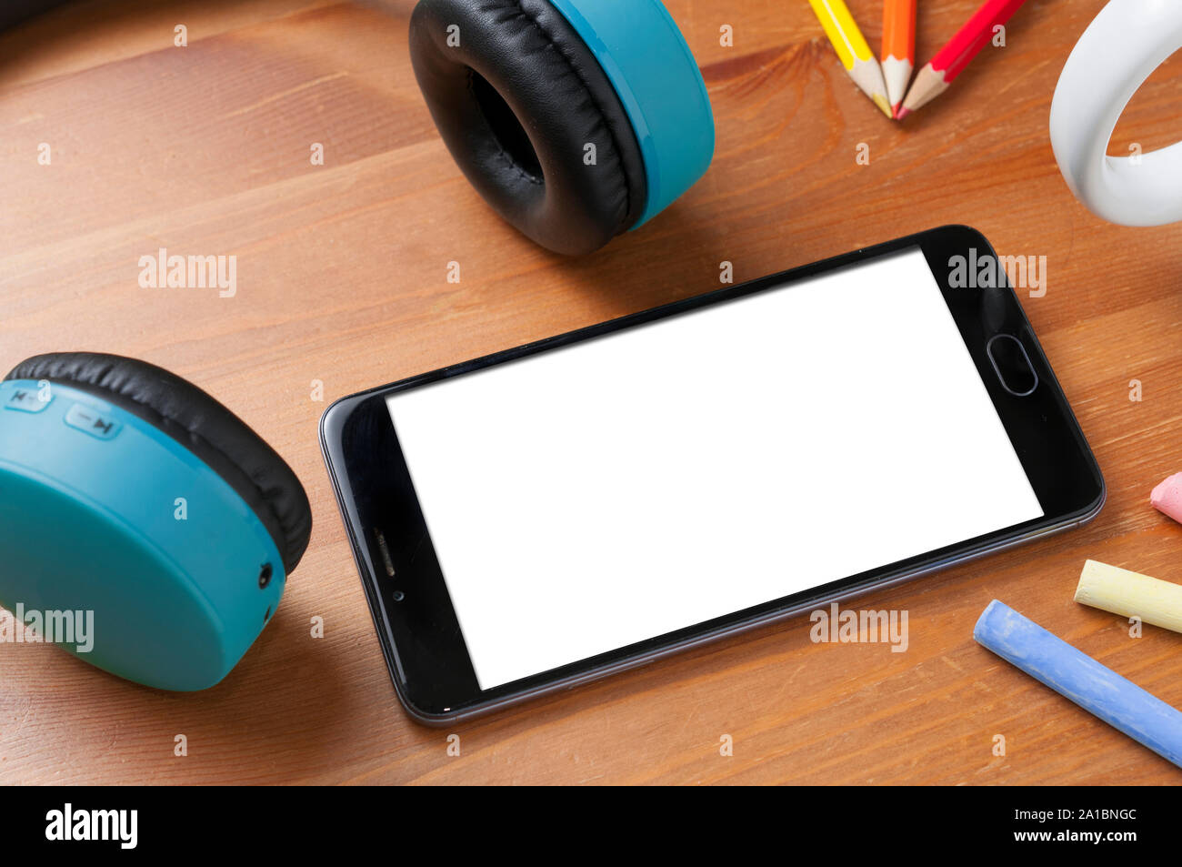 Smartphone écran vide sur une table en bois à côté d'une paire d'écouteurs sans fil, des crayons et des craies Banque D'Images