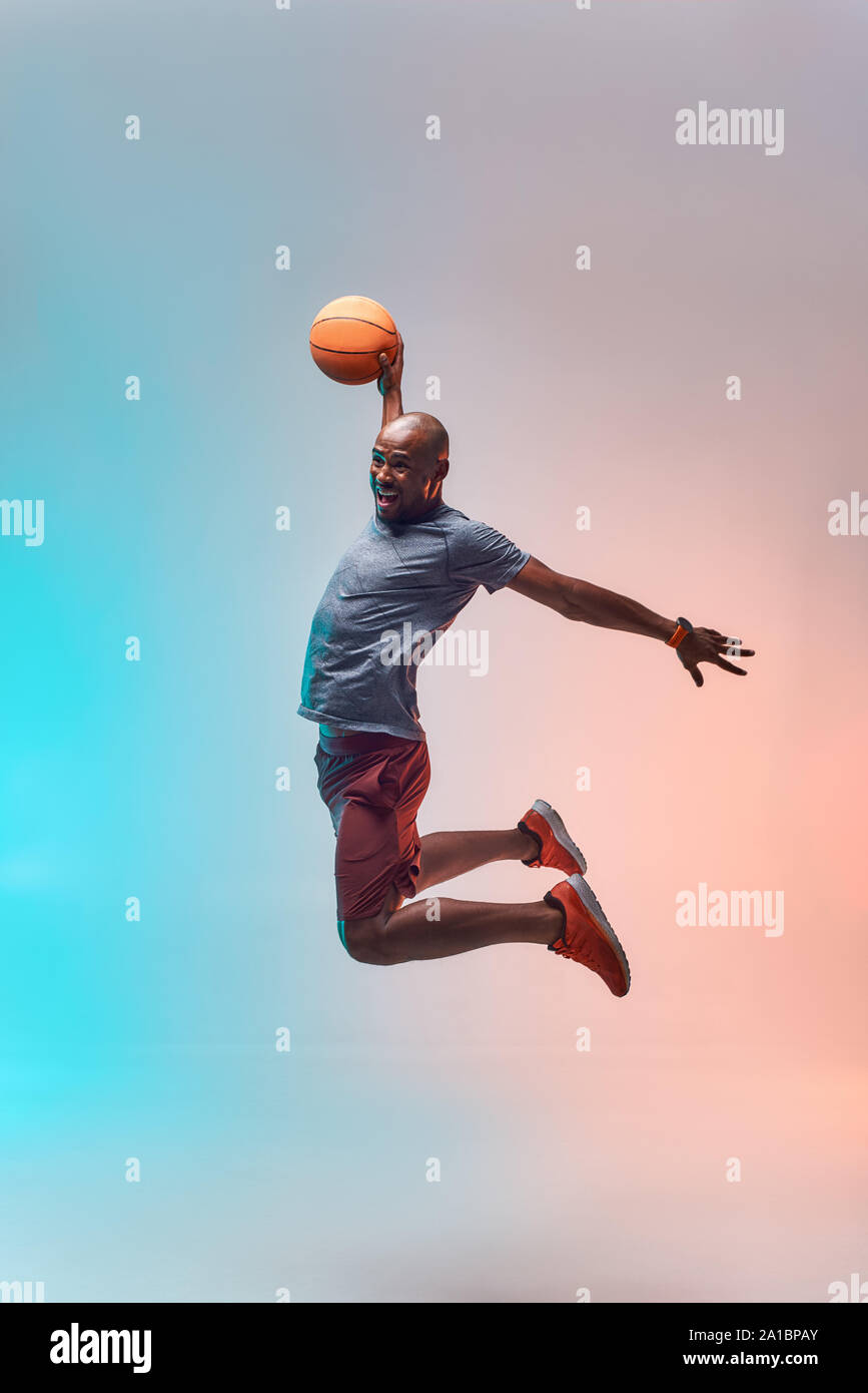 Joueur de basket-ball en action. Une longueur complète de jeunes sportifs africains jouant au basket-ball et sautant sur fond coloré. Mode de vie actif. Sport professionnel Banque D'Images