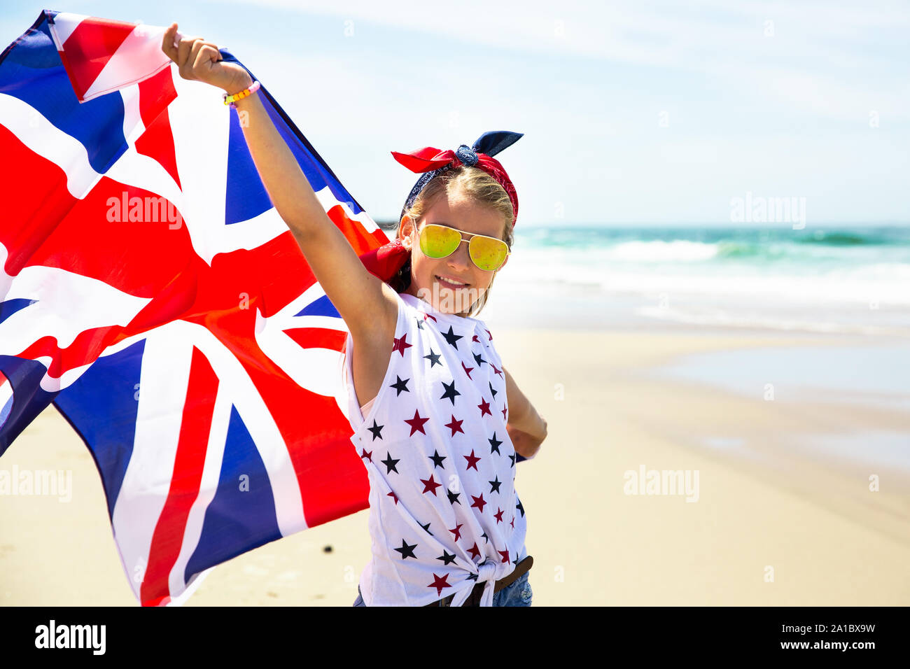 Happy girl britannique porte voletant bleu blanc rouge drapeau de la Grande-Bretagne, du Royaume-Uni et d'Irlande du Nord contre le ciel bleu et l'océan retour Banque D'Images