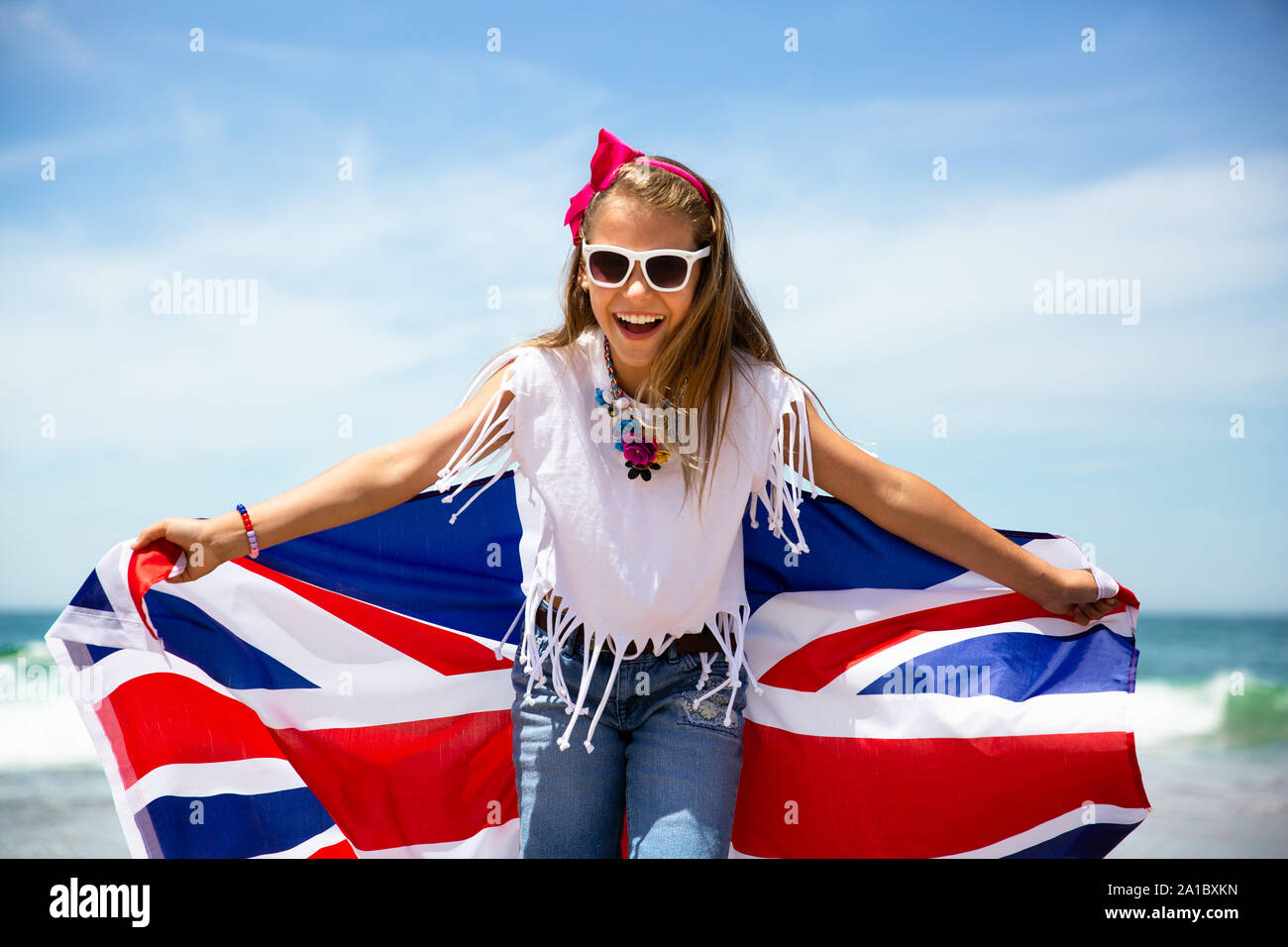 Happy girl britannique porte voletant bleu blanc rouge drapeau de la Grande-Bretagne, du Royaume-Uni et d'Irlande du Nord contre le ciel bleu et l'océan retour Banque D'Images