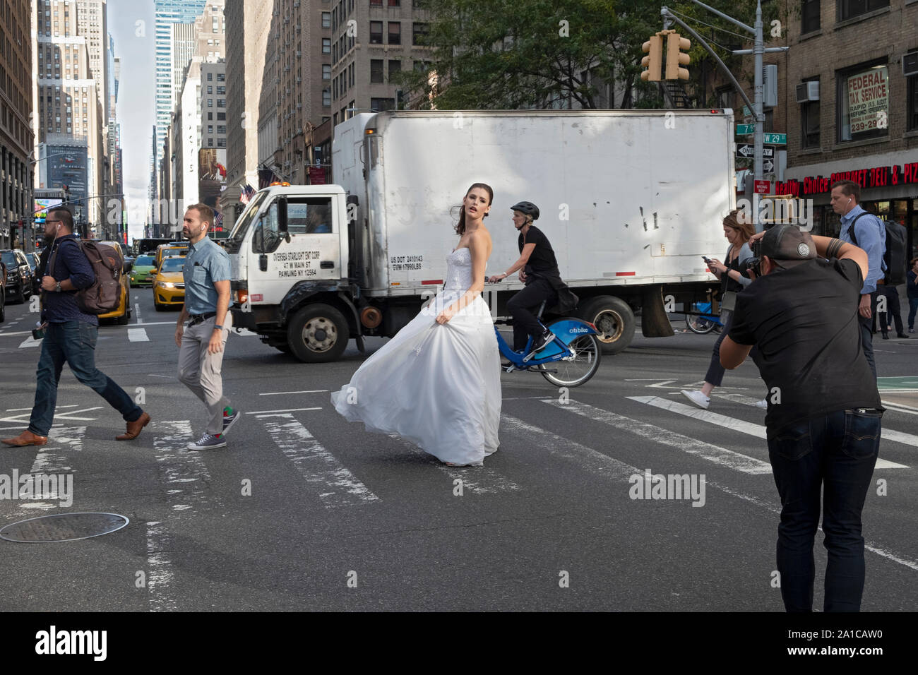 Un modèle d'une robe nuptiale pose pour des photos sur un coin de rue animée - 7th Ave. et West 29th Street - à Manhattan, New York City. Banque D'Images