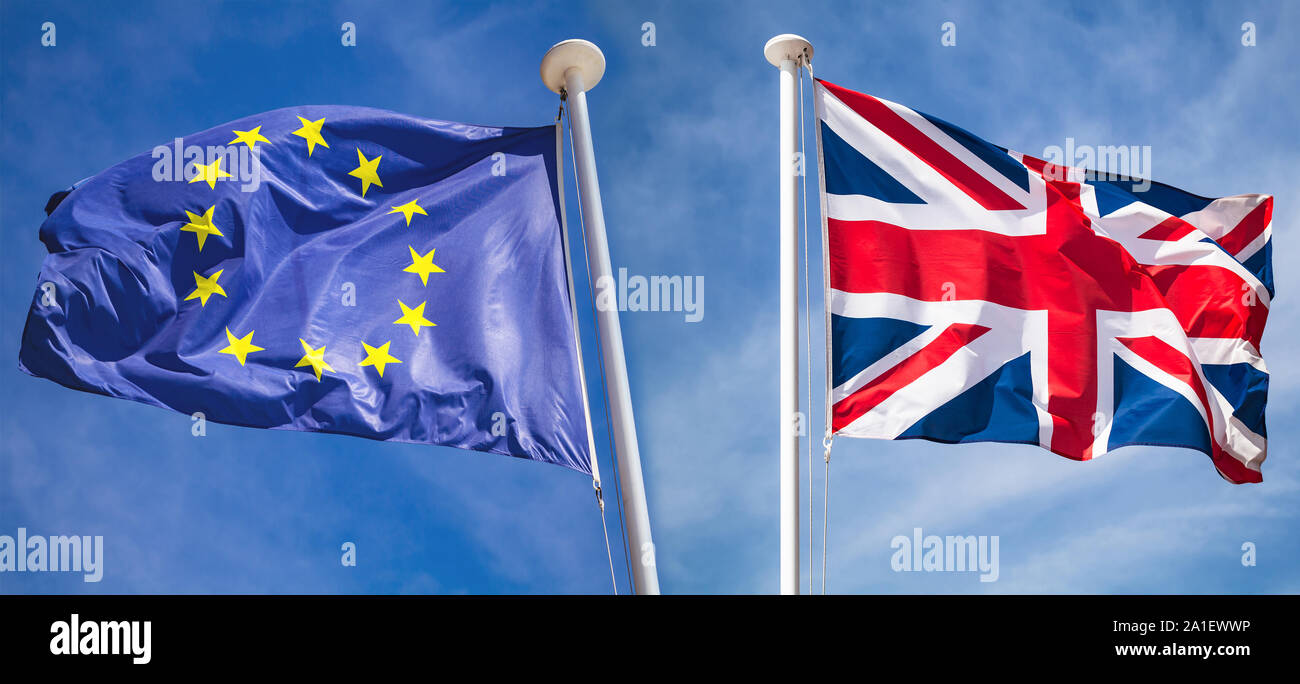 Brexit concept. Le drapeau national du Royaume-Uni et de brandir le drapeau de l'Union européenne sur le vent dans des directions opposées sur fond de ciel bleu Banque D'Images