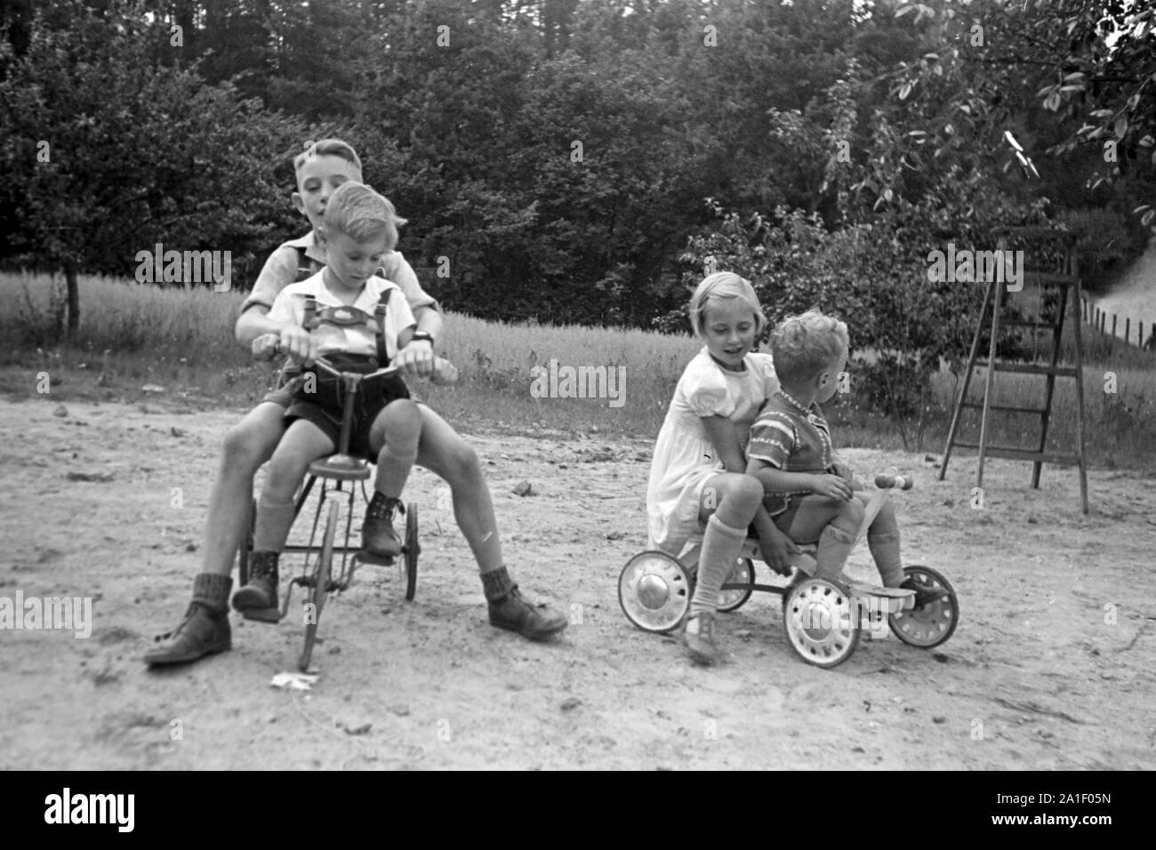 Kinder spielen mit und Rouleau Dreirad auf einem Spielplatz, Deutschland 1939. Les enfants avec des tricycles et scooters sur une aire de jeux, Allemagne 1939. Banque D'Images