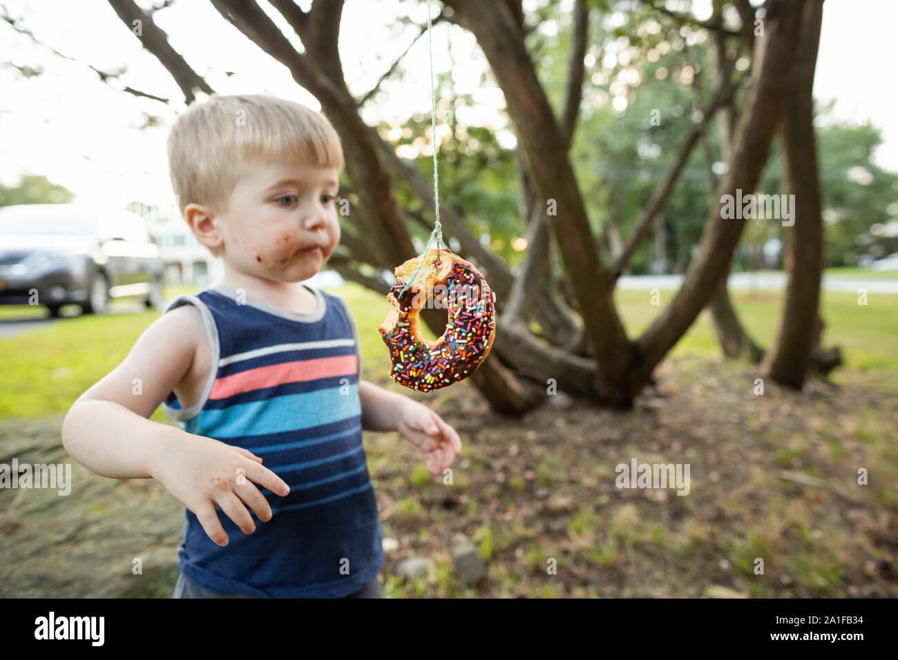 Bébé garçon se tient à côté d'une chaîne de beignes pendant party Banque D'Images