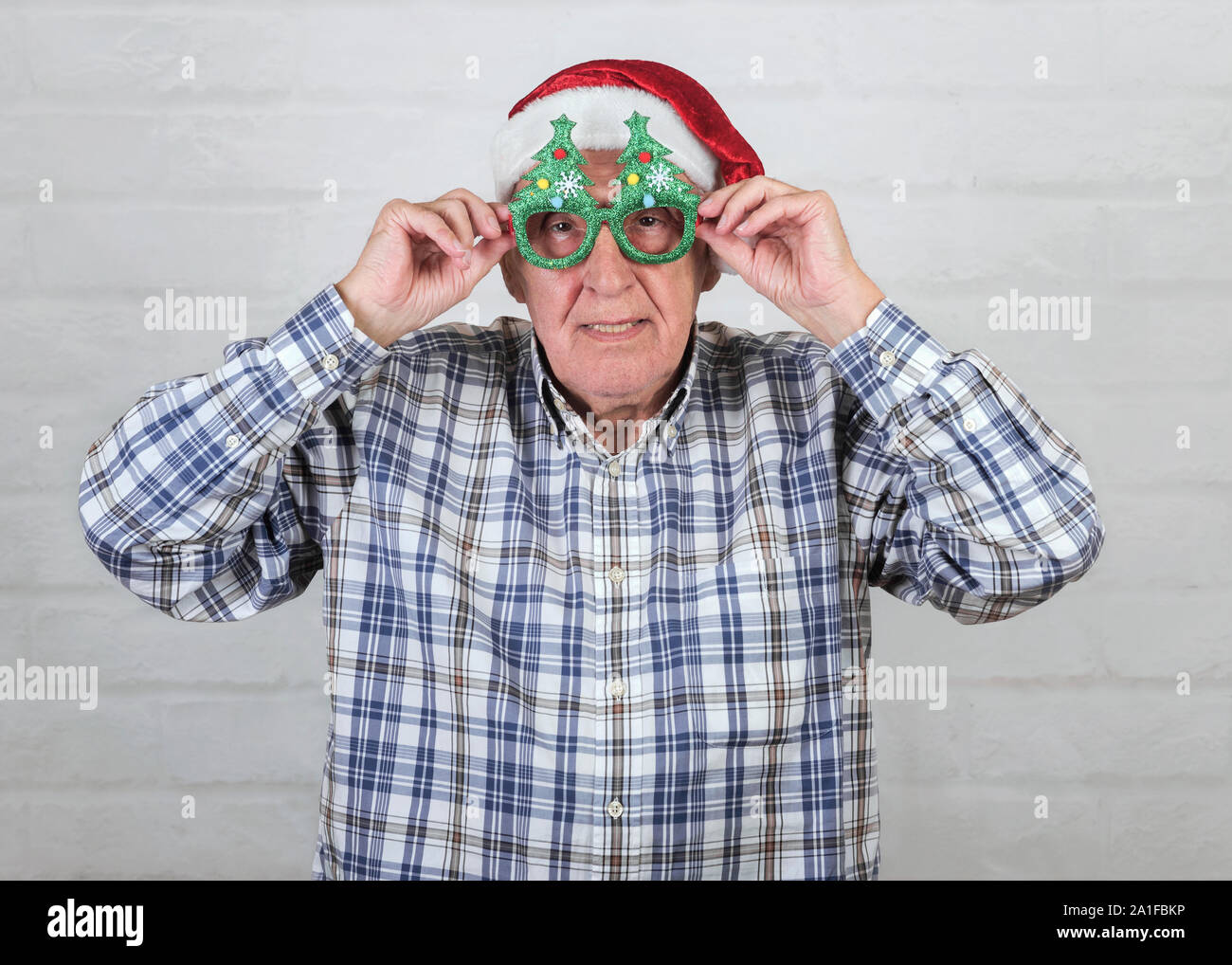 Grand-père Wearing Christmas Santa Claus Hat et drôles de lunettes sur fond brique Banque D'Images