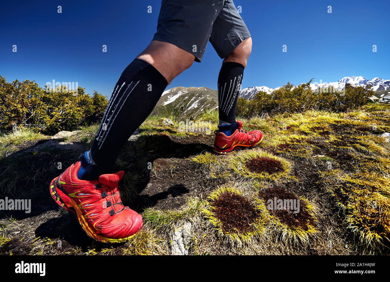 Close up of hiker jambes en chaussures rouges sont l'escalade dans les montagnes au fond de ciel bleu. Mode de vie sain. Voyage en plein air concept. Banque D'Images